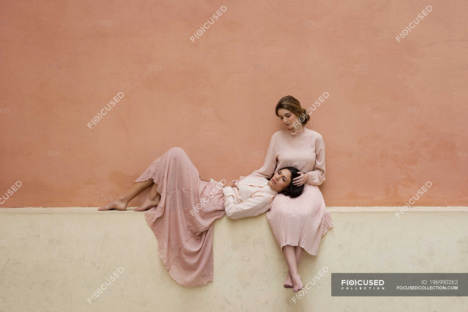 Brunette Woman Lying On Knees Of Girlfriend Sitting At Orange Wall — Horizontal Attractive 3366