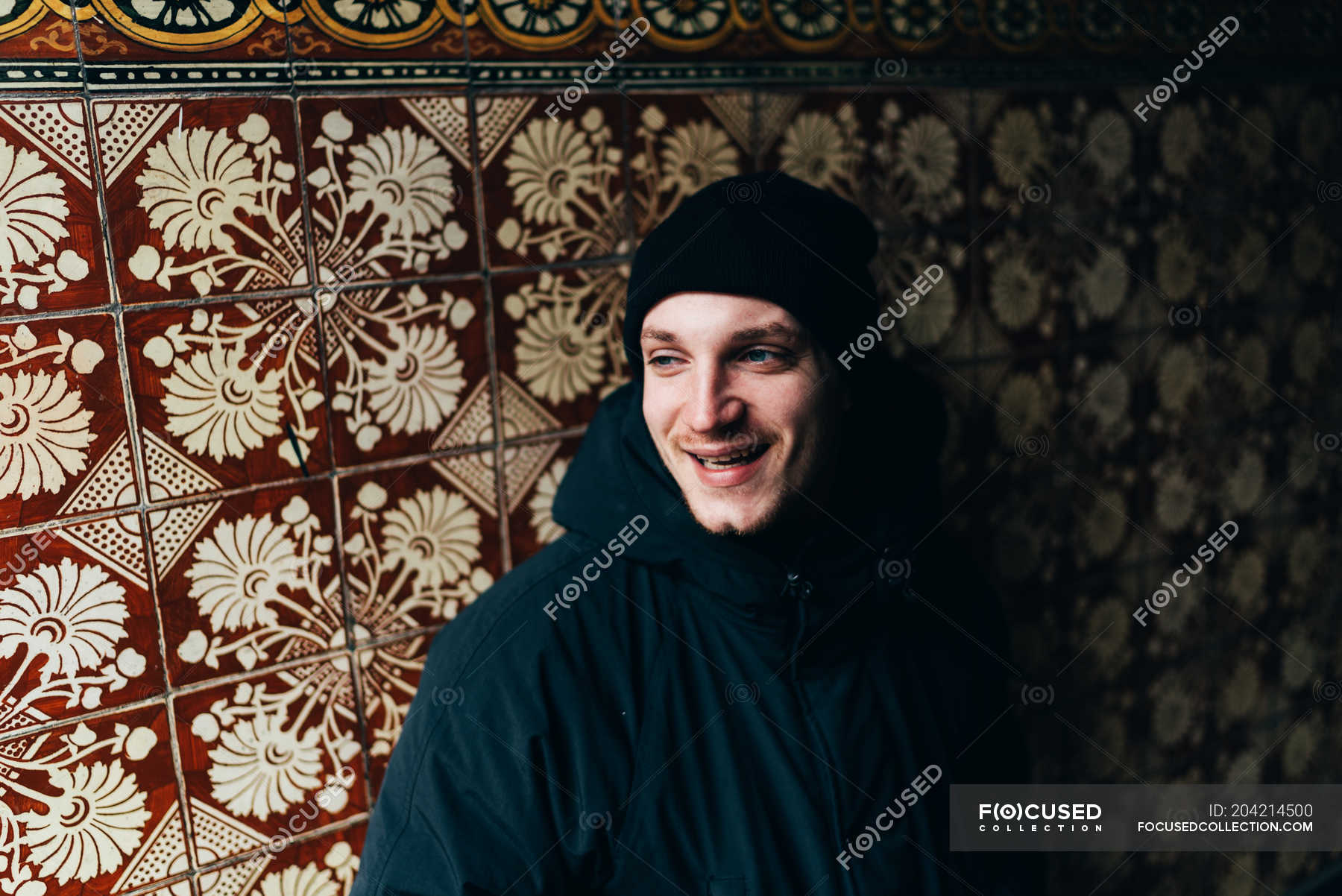 Handsome young man standing at wall with yellow and brown tiles ...