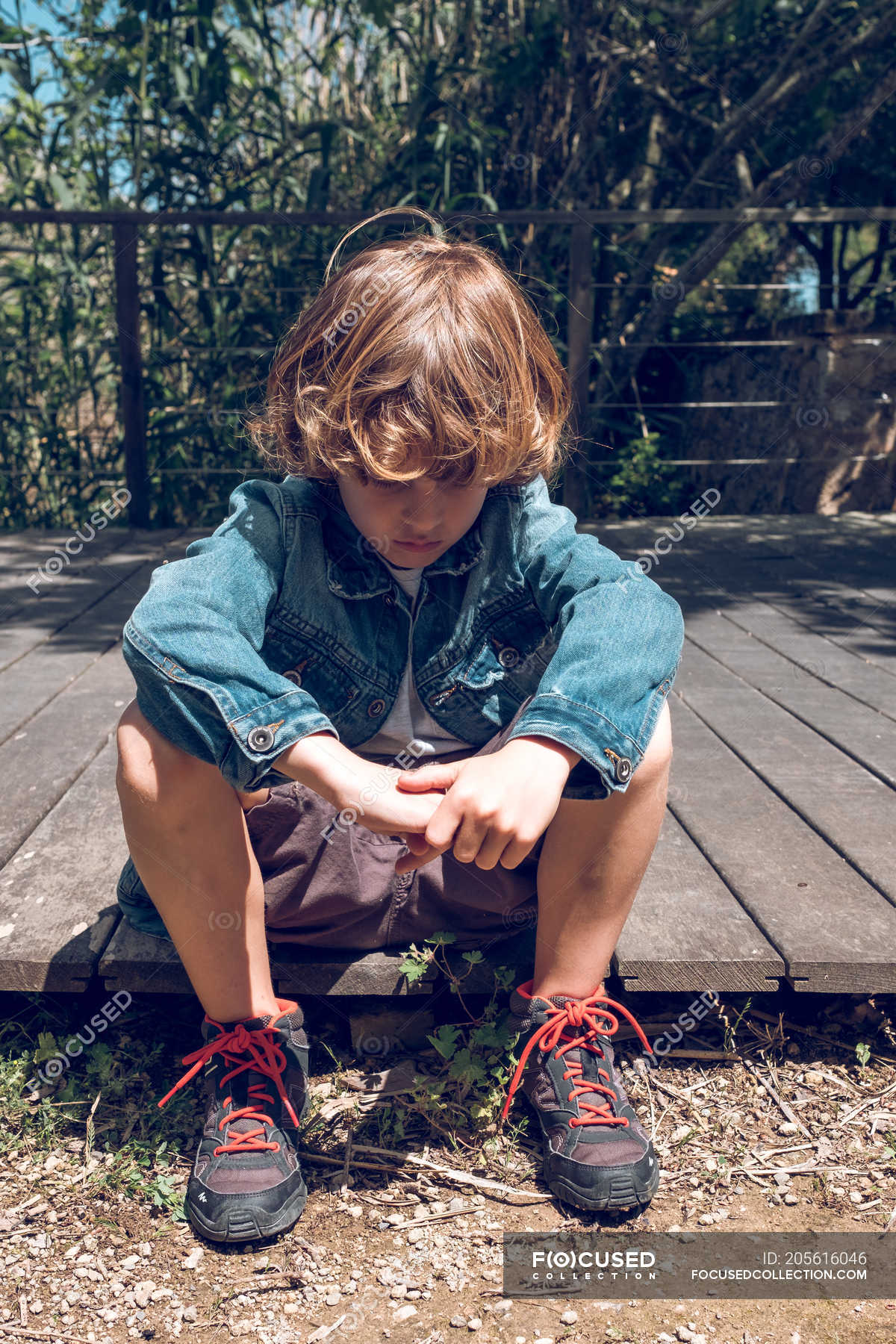 Cute Elementary Age Boy With Curly Blond Hair Sitting On Wooden