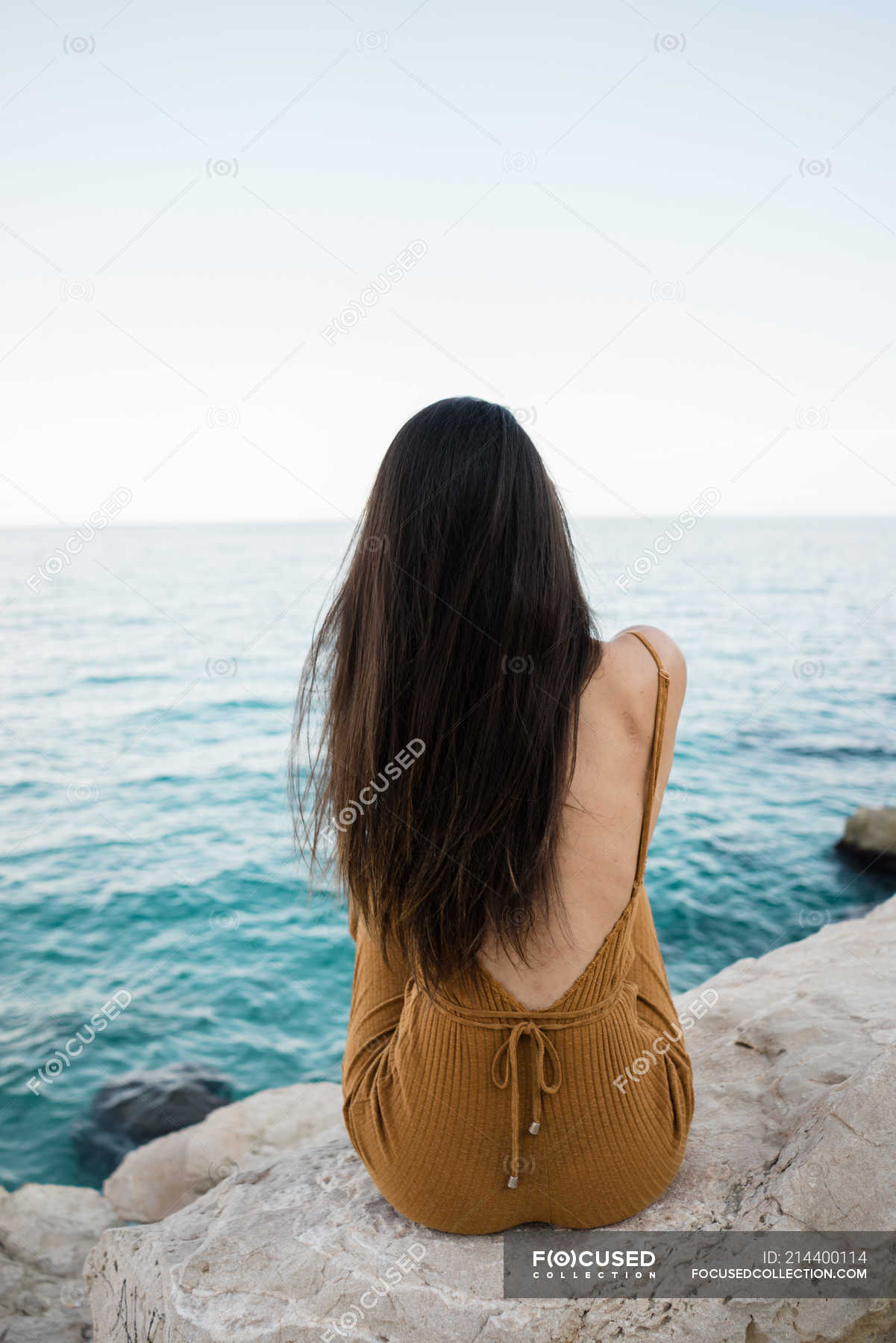 Rear view of woman with long hair sitting on rocky shoreline — style, Black  Hair - Stock Photo | #214400114