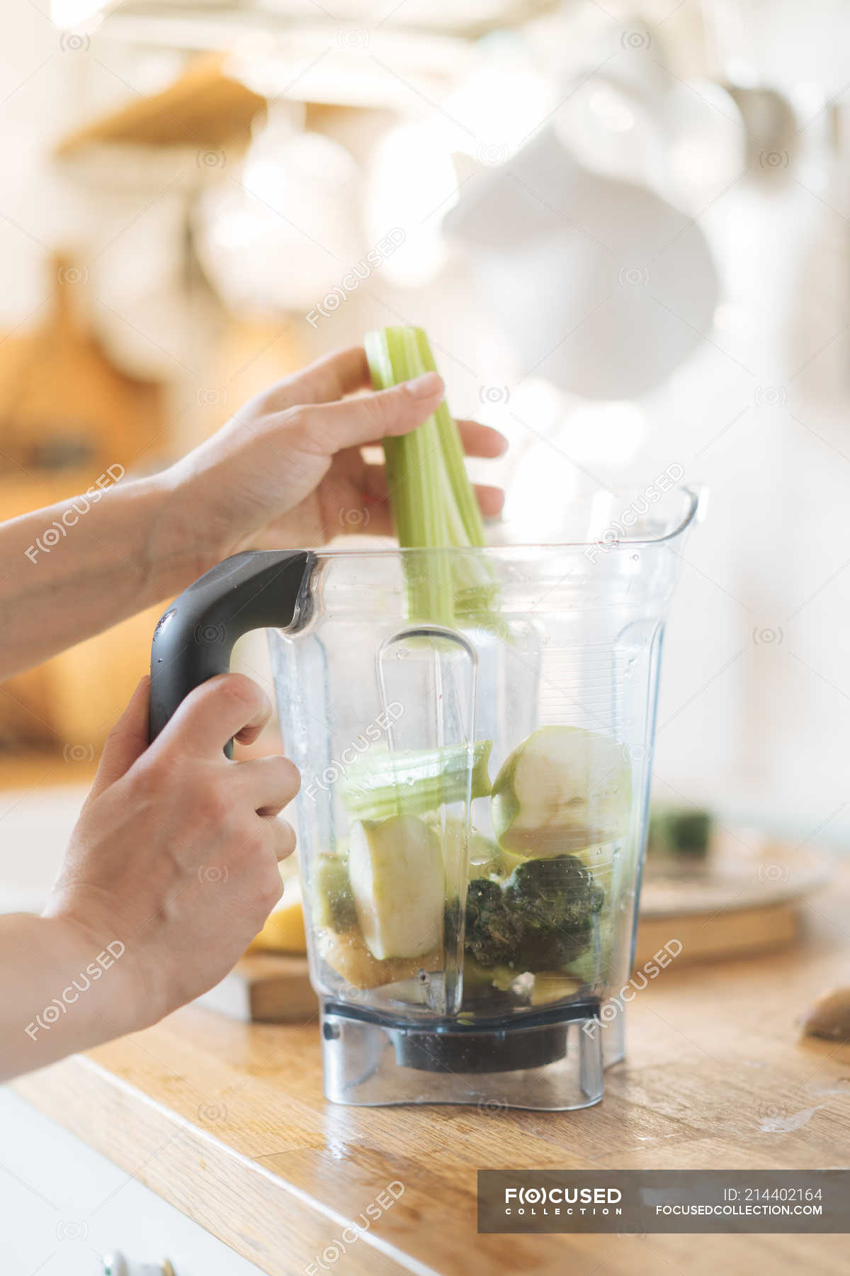 Female hands putting celery in blender bowl for green smoothie — raw