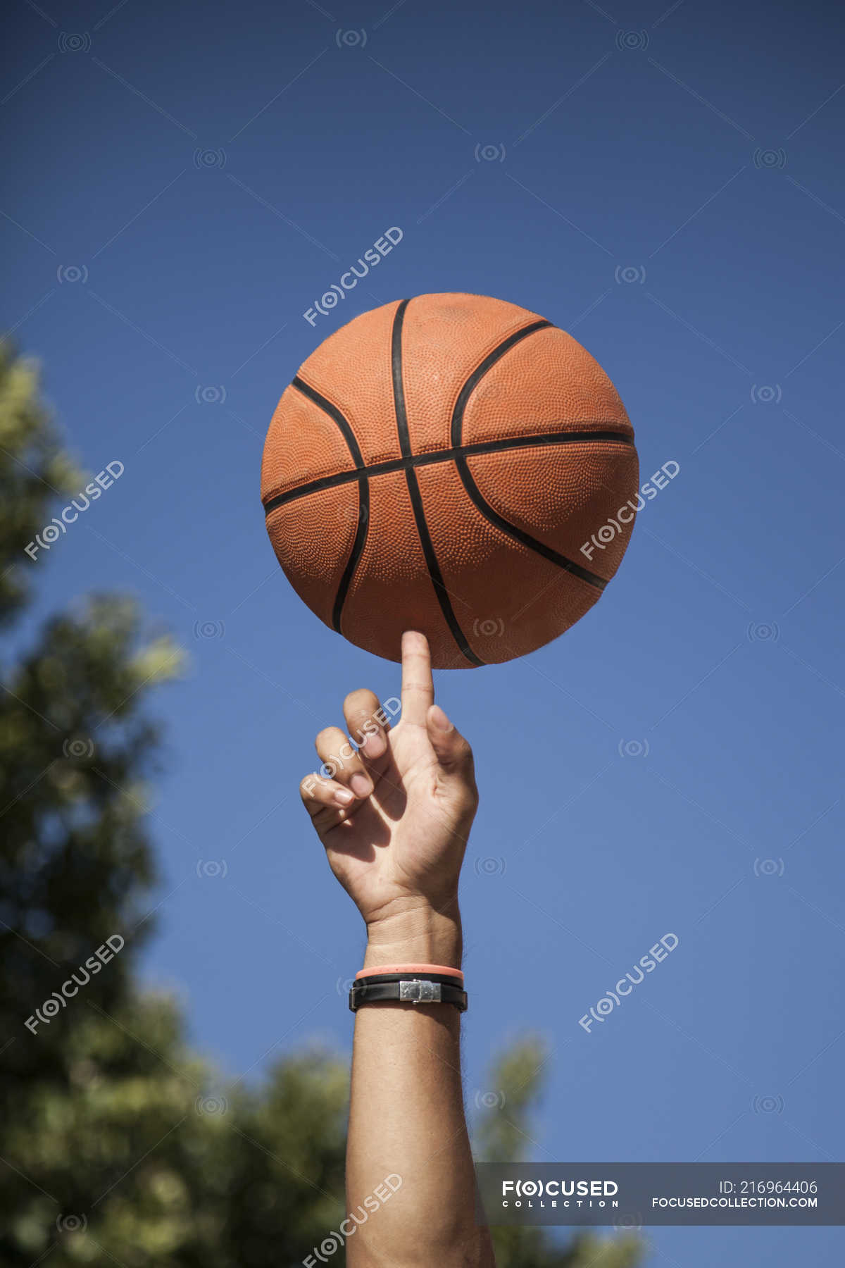 Male hand spinning basketball on finger with blue sky on background ...