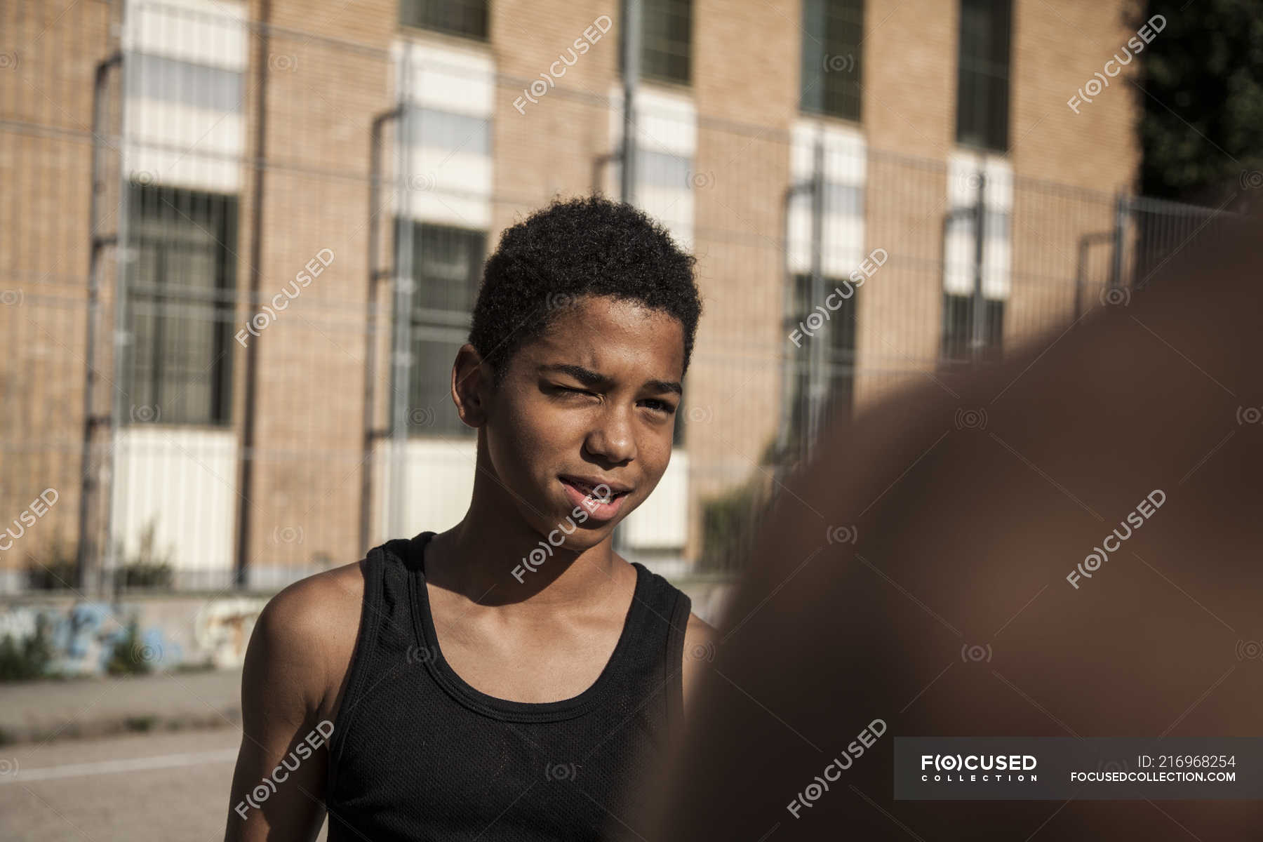 Afro young boy squinting outdoors against building — cropped image ...