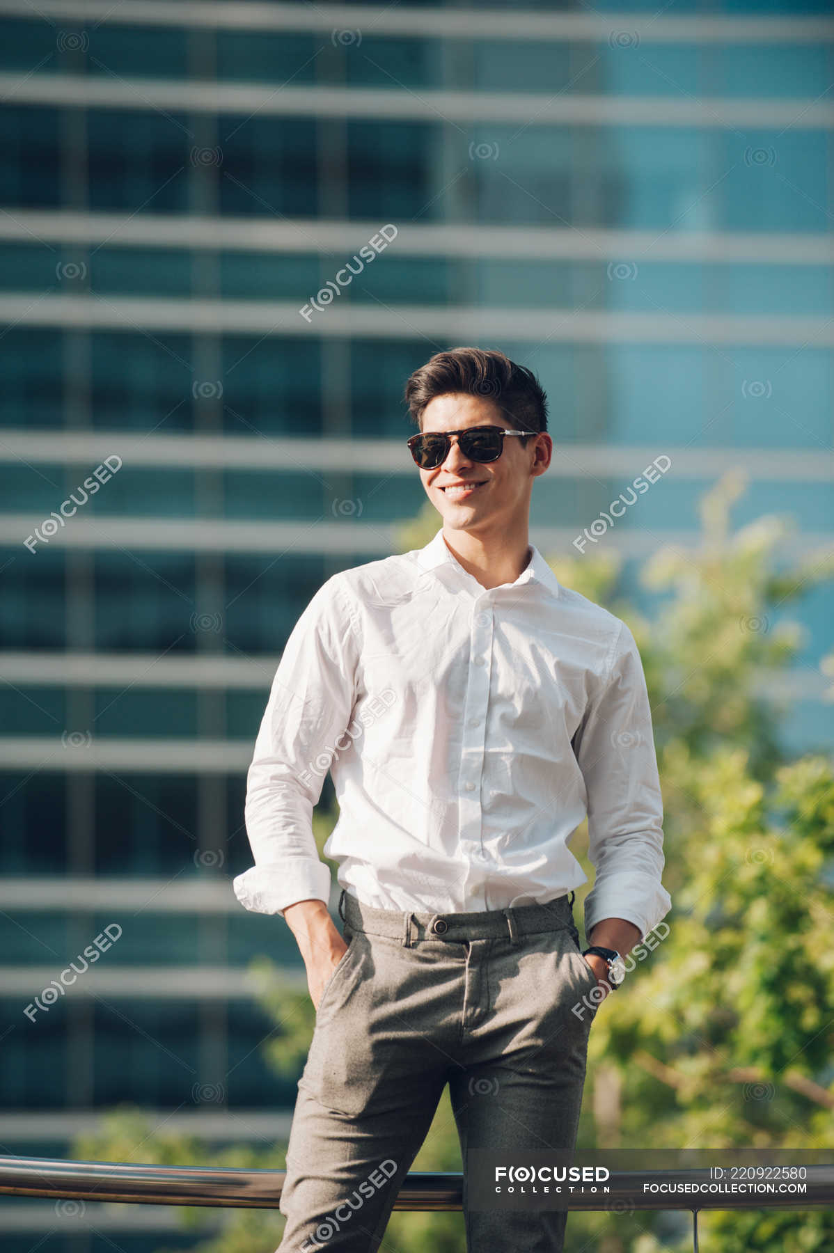 Positive businessman standing against modern building — smiling, street ...