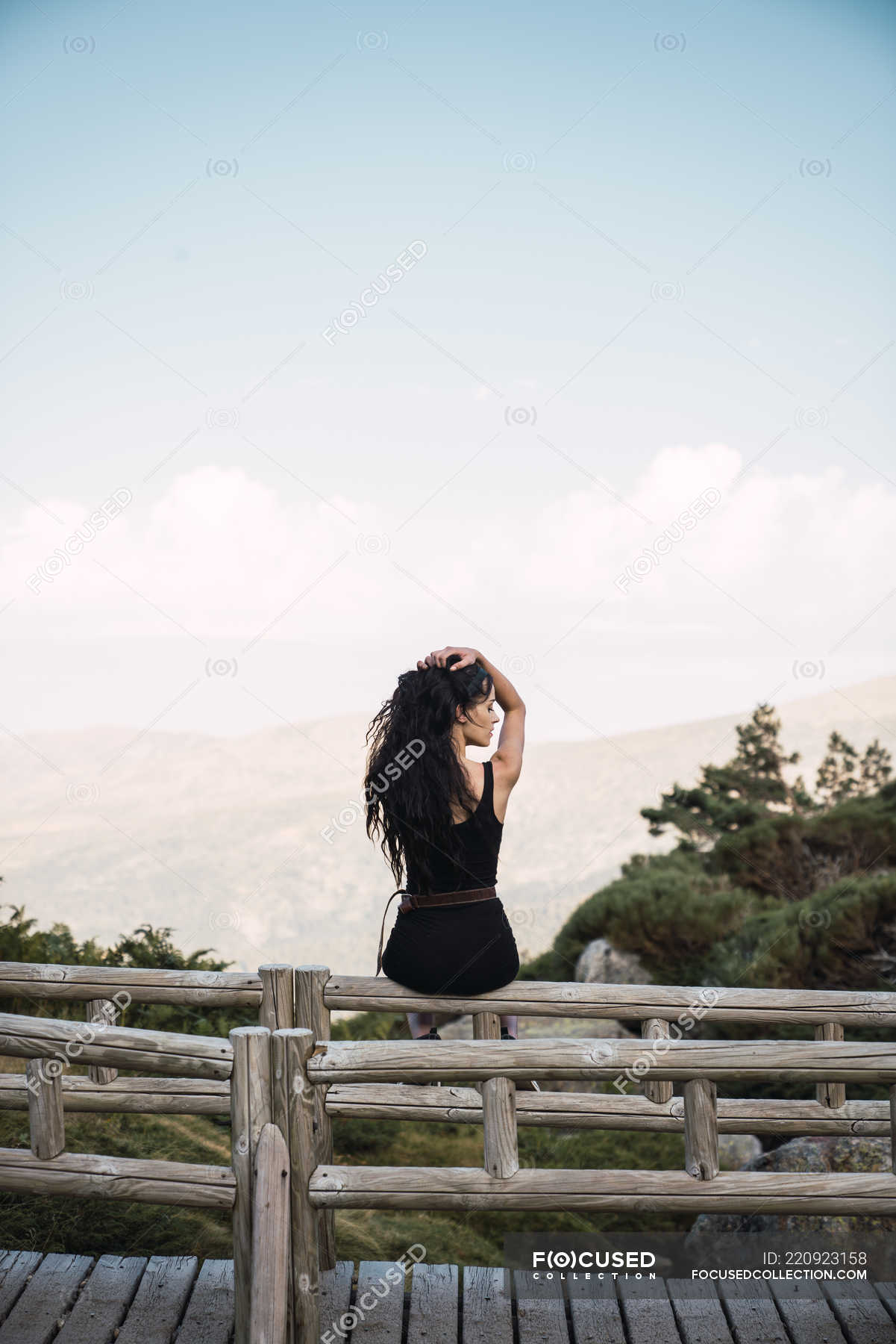 Back view of sensual woman in black with long hair sitting on wooden fence  above picturesque valley landscape — spain, walkway - Stock Photo |  #220923158