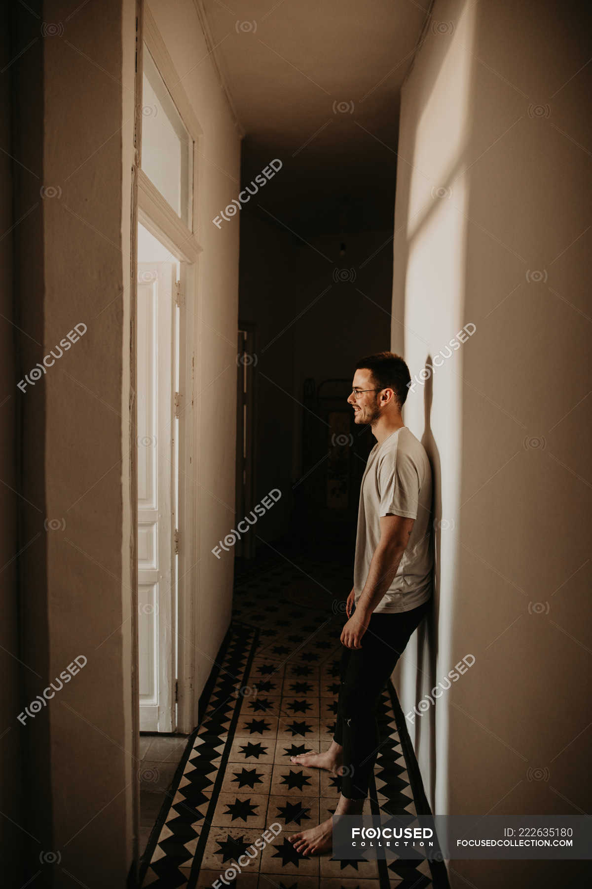 side-view-of-cheerful-man-leaning-on-wall-and-looking-away-in-hall-at