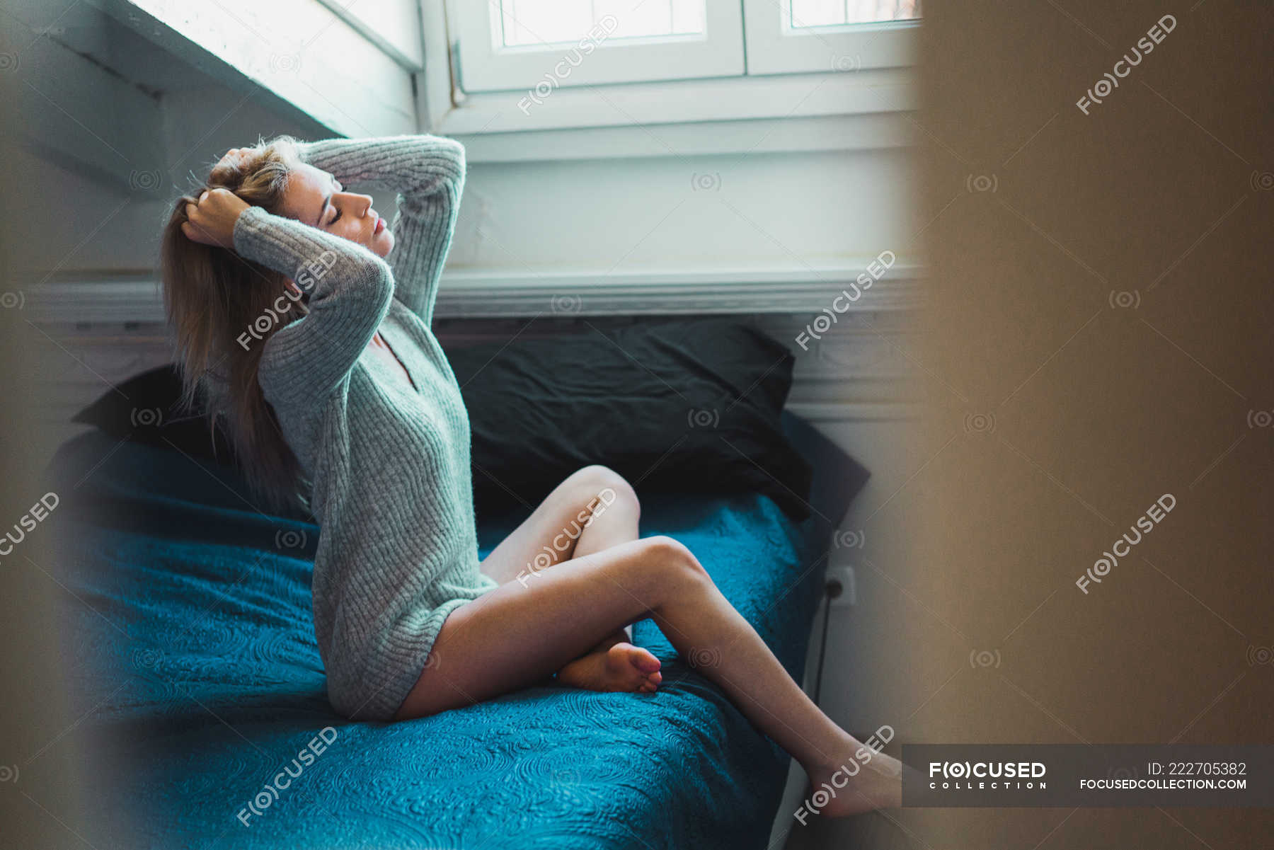 Young Woman In Sweater With Hands In Hair Relaxing On Bed At Home