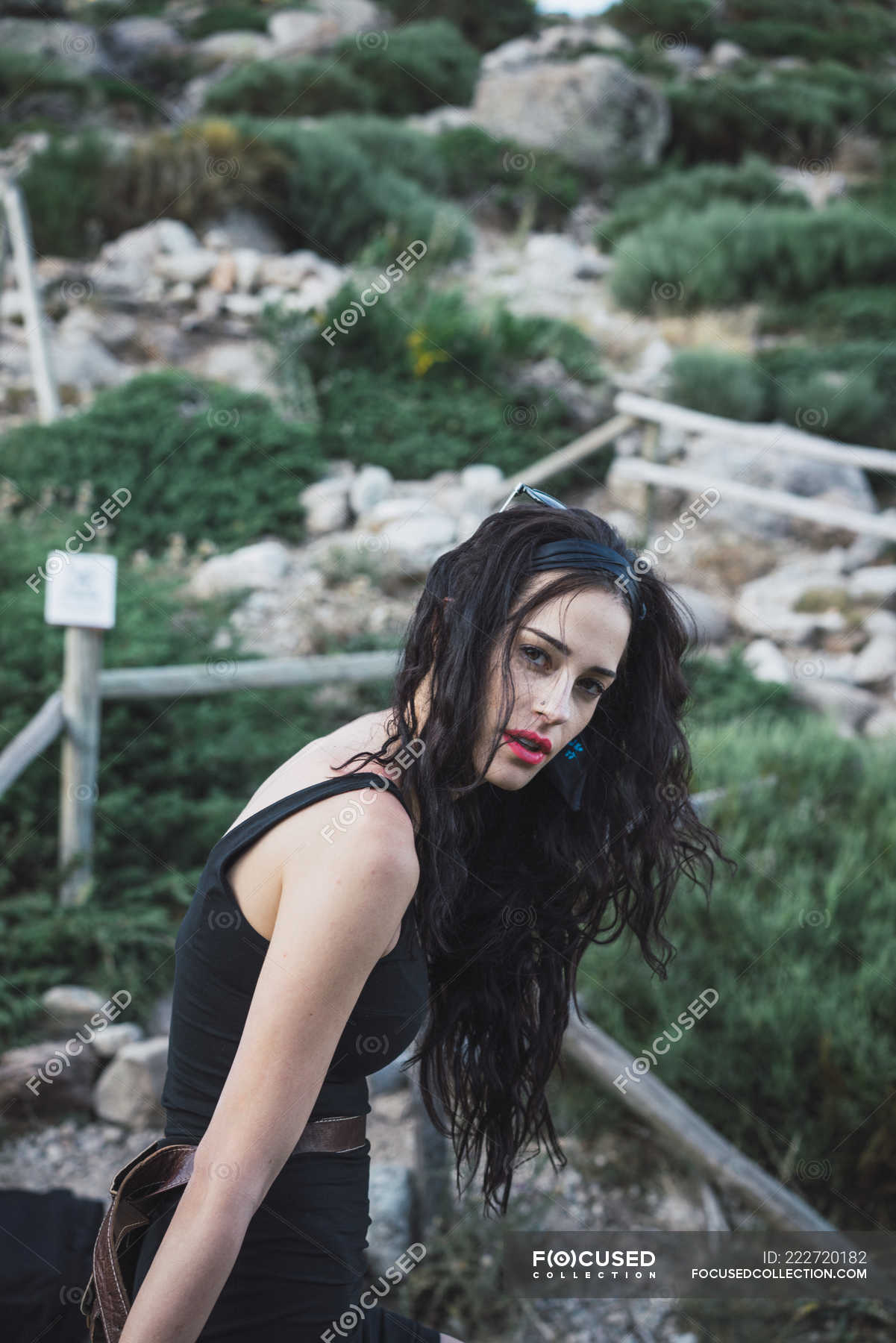 Young Woman Leaning On Fence In Nature And Looking At Camera — Side