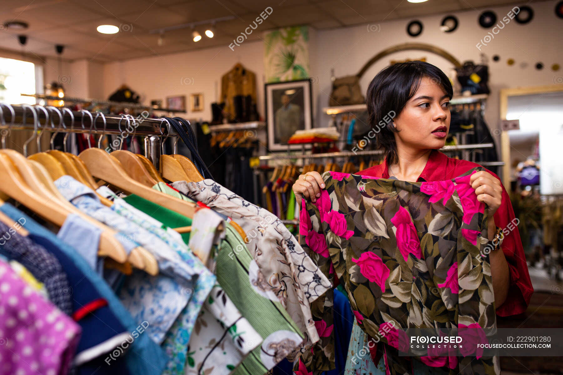 Pretty young female smiling and picking garment from clothes rail while ...