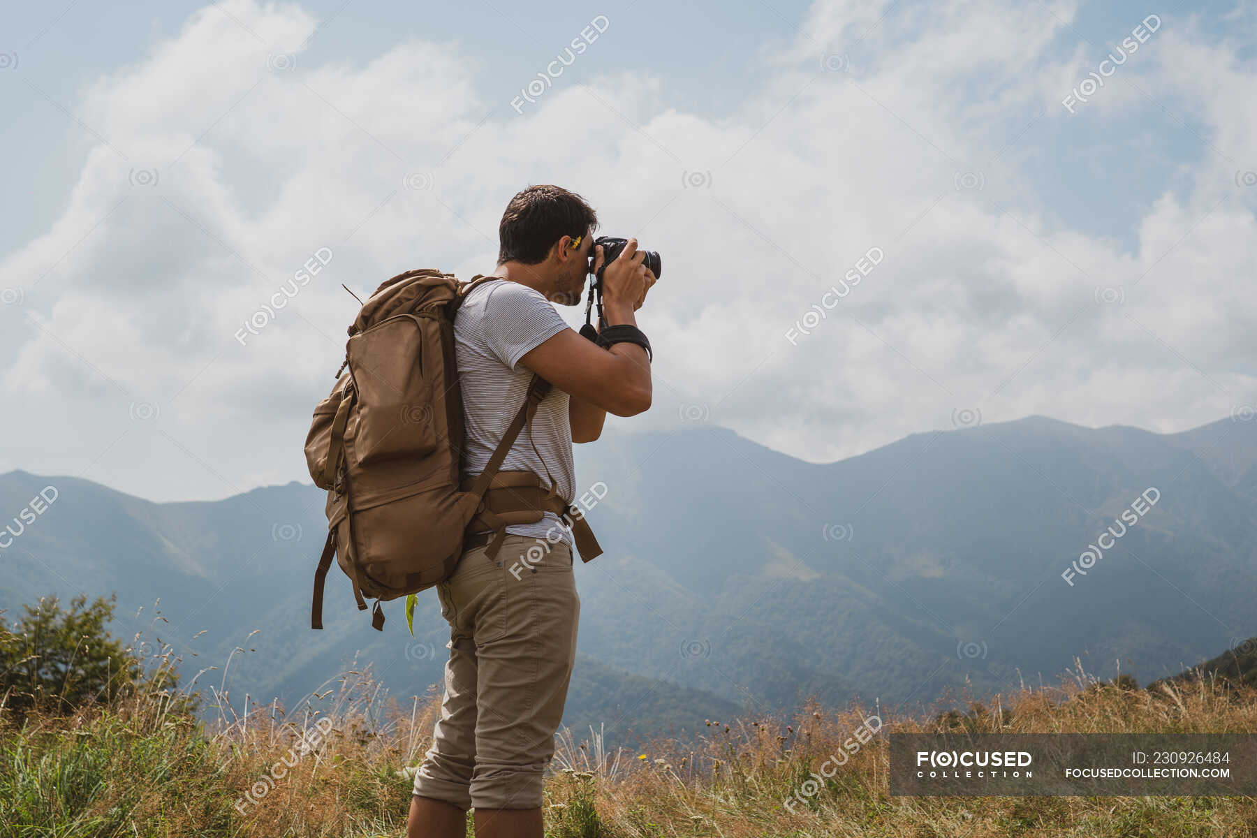 Back view of man with backpack using professional camera to make photos ...