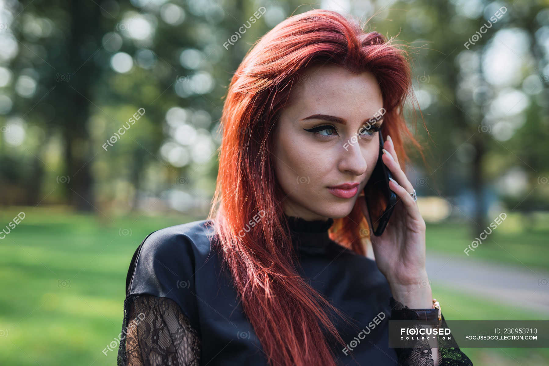 young-woman-with-ginger-hair-talking-on-smartphone-in-sunny-park