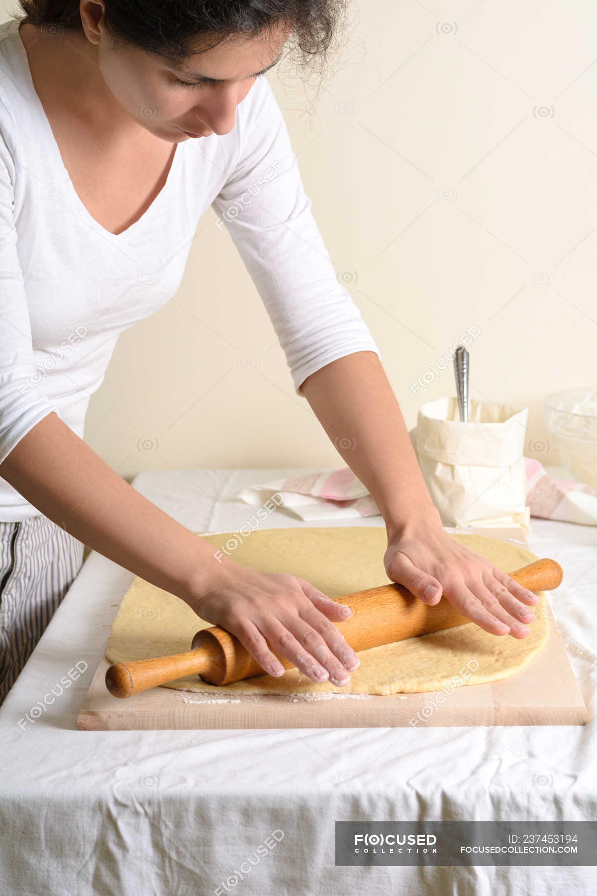 Pretty female using wooden rolling pin to rolling fresh dough in cozy ...