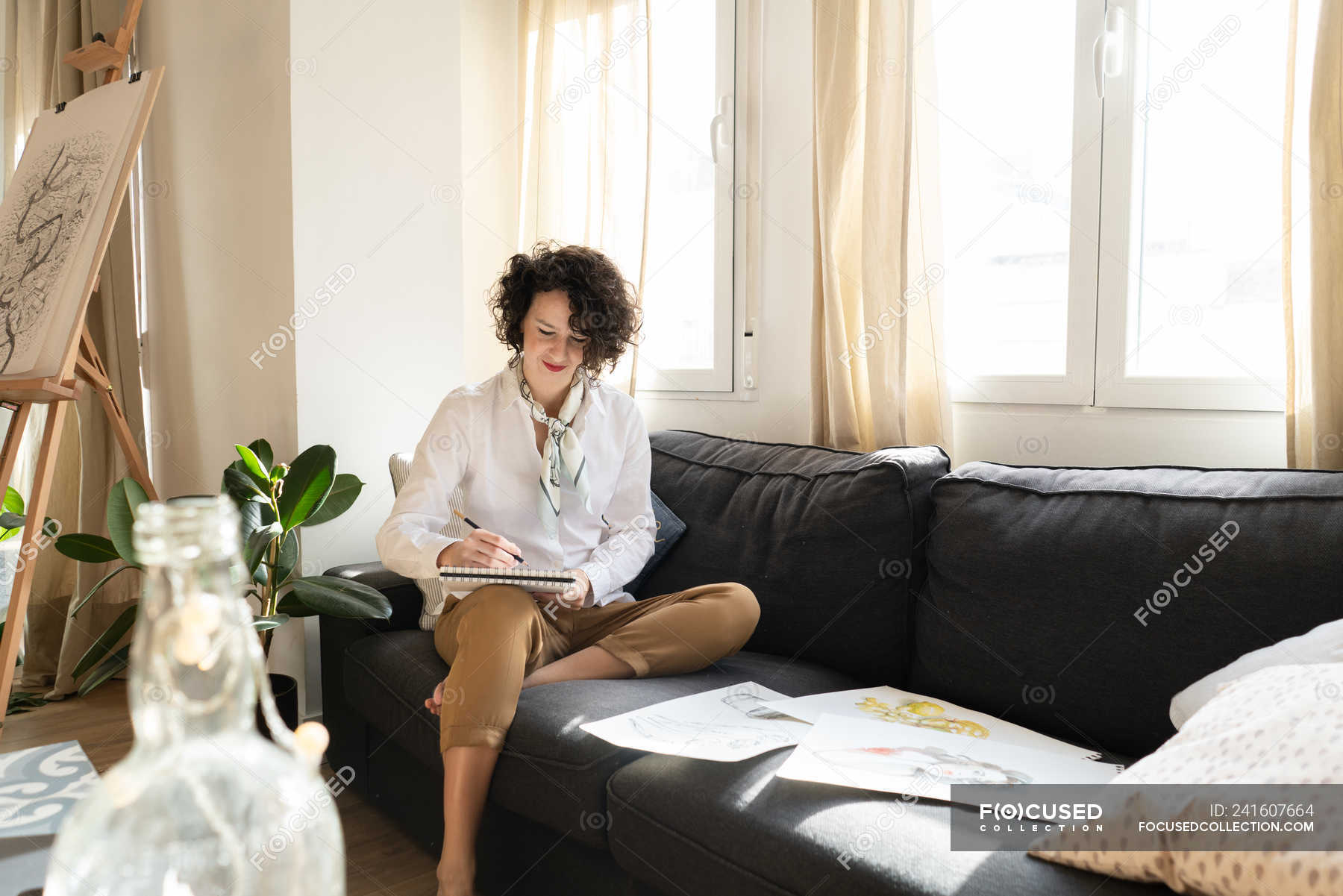 Woman writing on paper on sofa in room — glass, positive Stock Photo