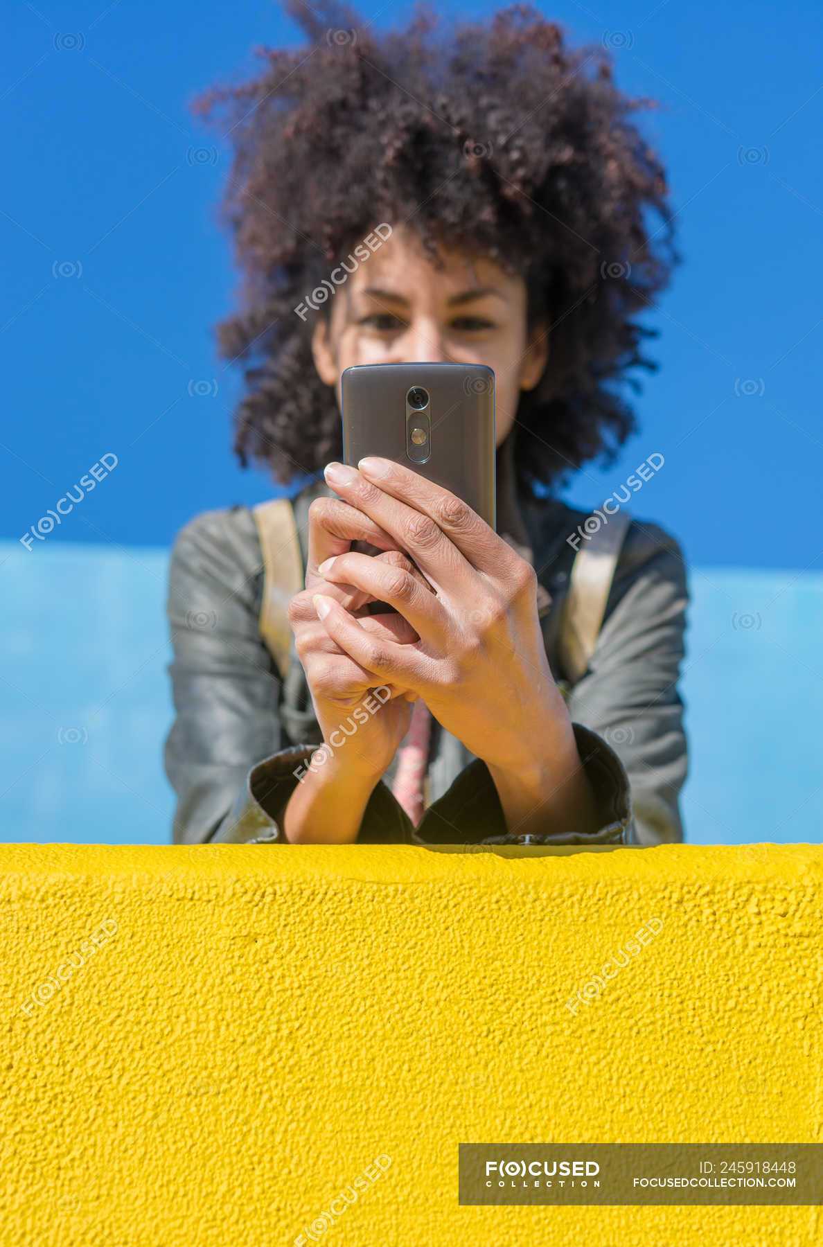 Black Woman With Afro Hair Leaning Against Brightly Colored Walls While