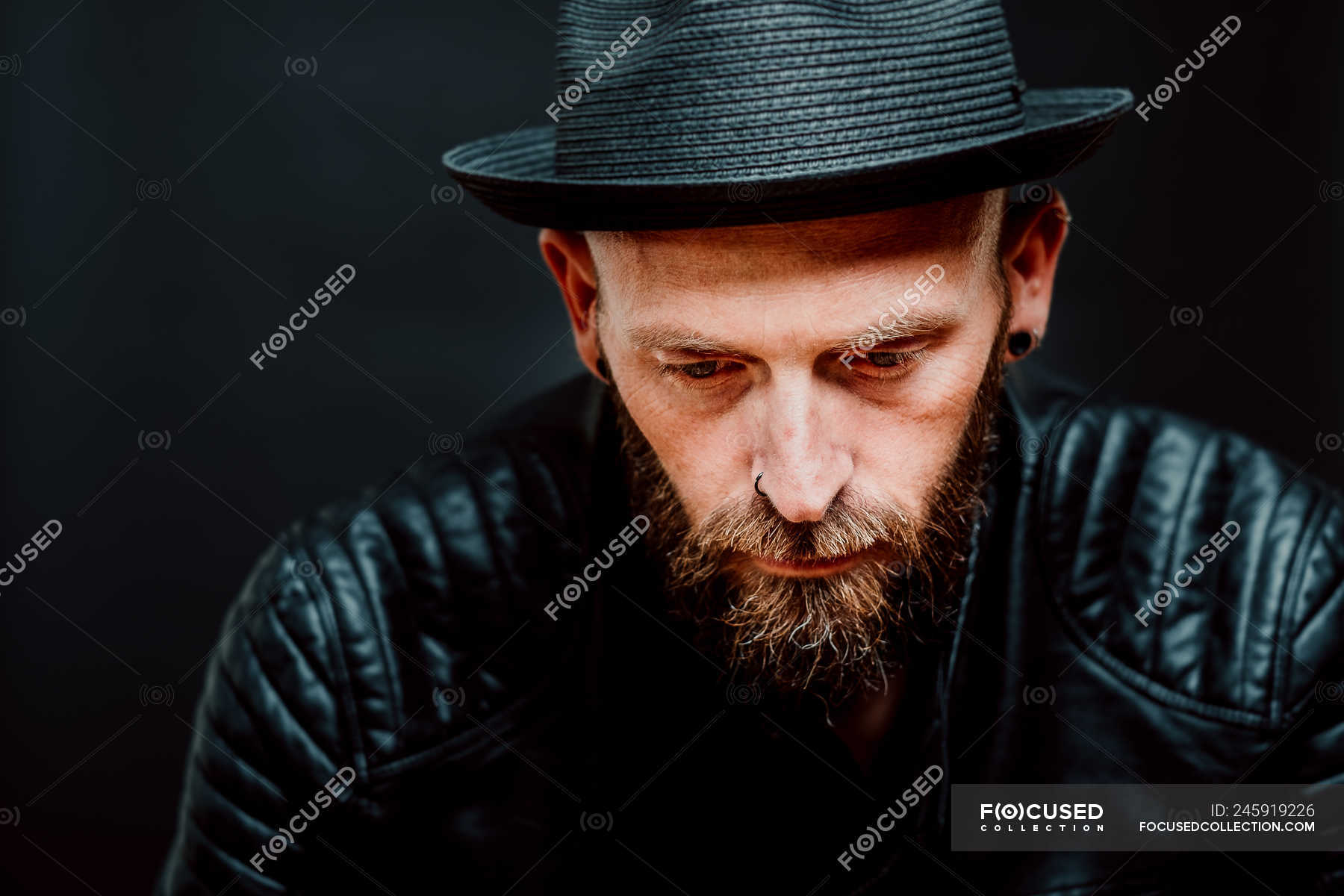 Cool Hipster In Hat And Leather Jacket Looking Down On Black Background — Confident Trendy