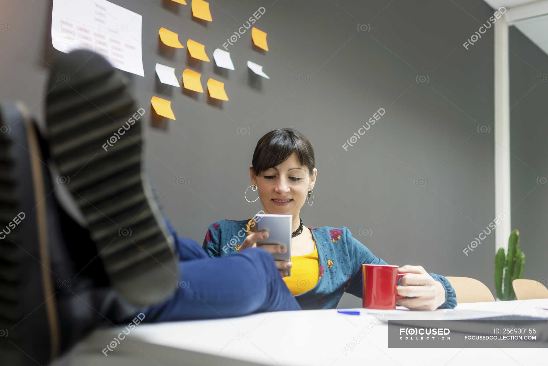 Female Manager With Mug Of Hot Beverage Using Smartphone While Female Manager With Mug Of Hot Beverage