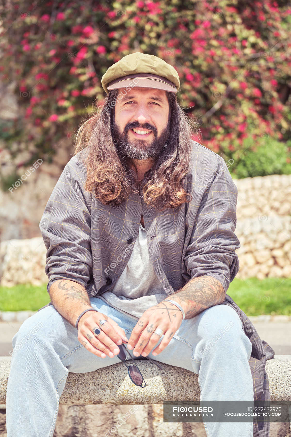 Stylish bearded man with long hair sitting in park — trendy, outfit - Stock  Photo | #272472970