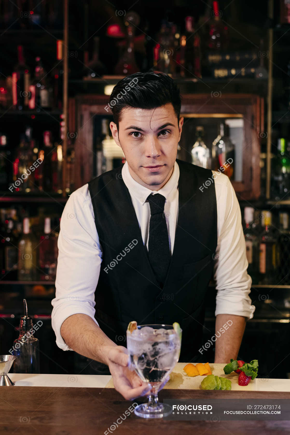 Young elegant barman working behind a bar counter mixing drinks with