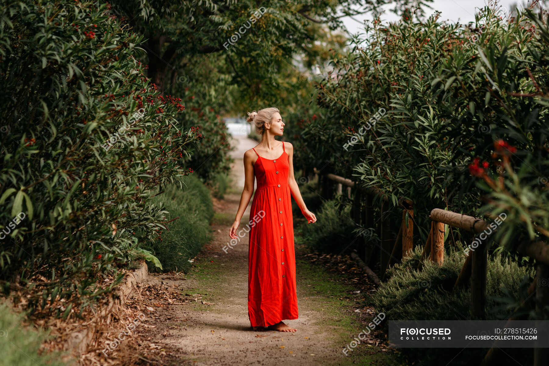 Side View Of Attractive Blonde Dressed In Red Sensually Posing With Closed Eyes Among Green 