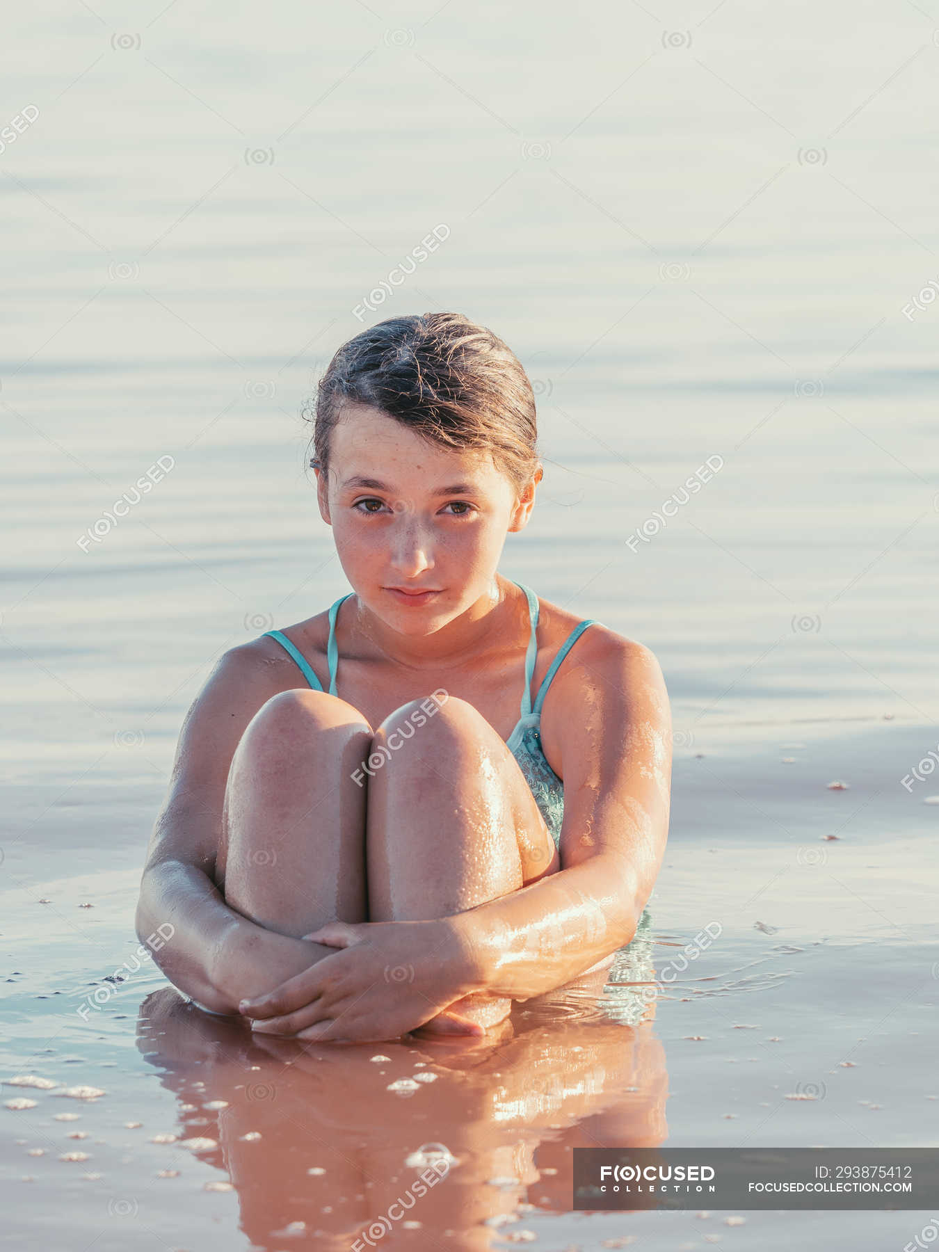 Раздетая молодая девушка сидит у воды