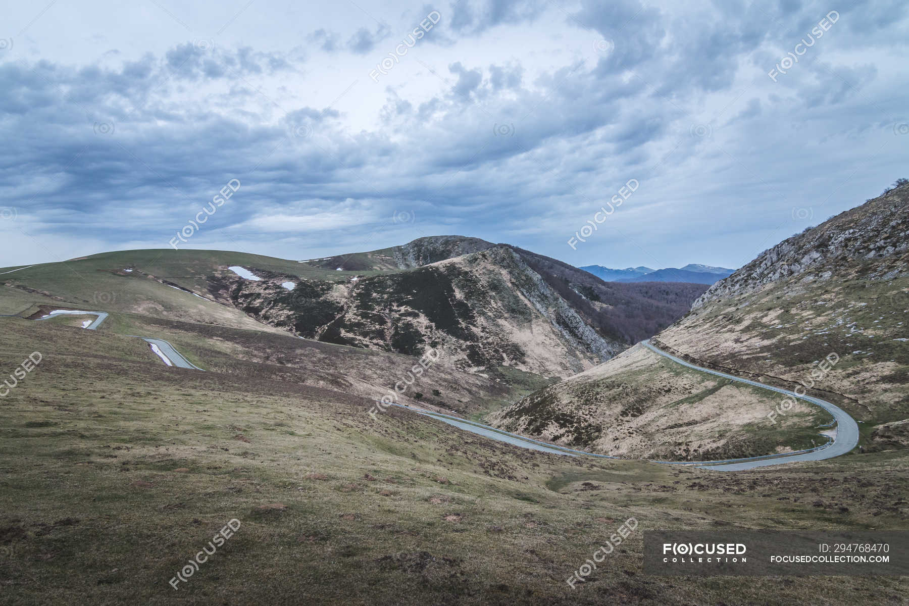 narrow-winding-road-going-on-slopes-of-grassy-hills-on-cloudy-day-in