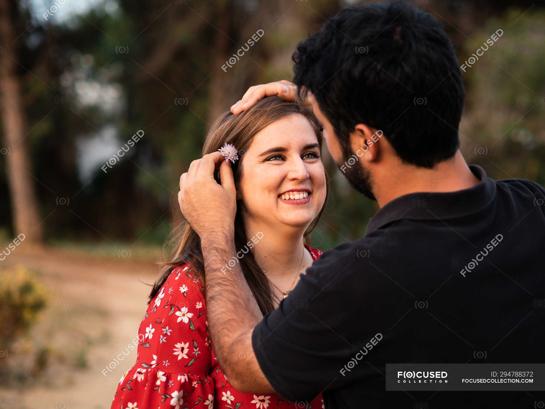 Man smiling at wife in blurred nature and putting on flower in hair —  husband, girlfriend - Stock Photo | #294788372