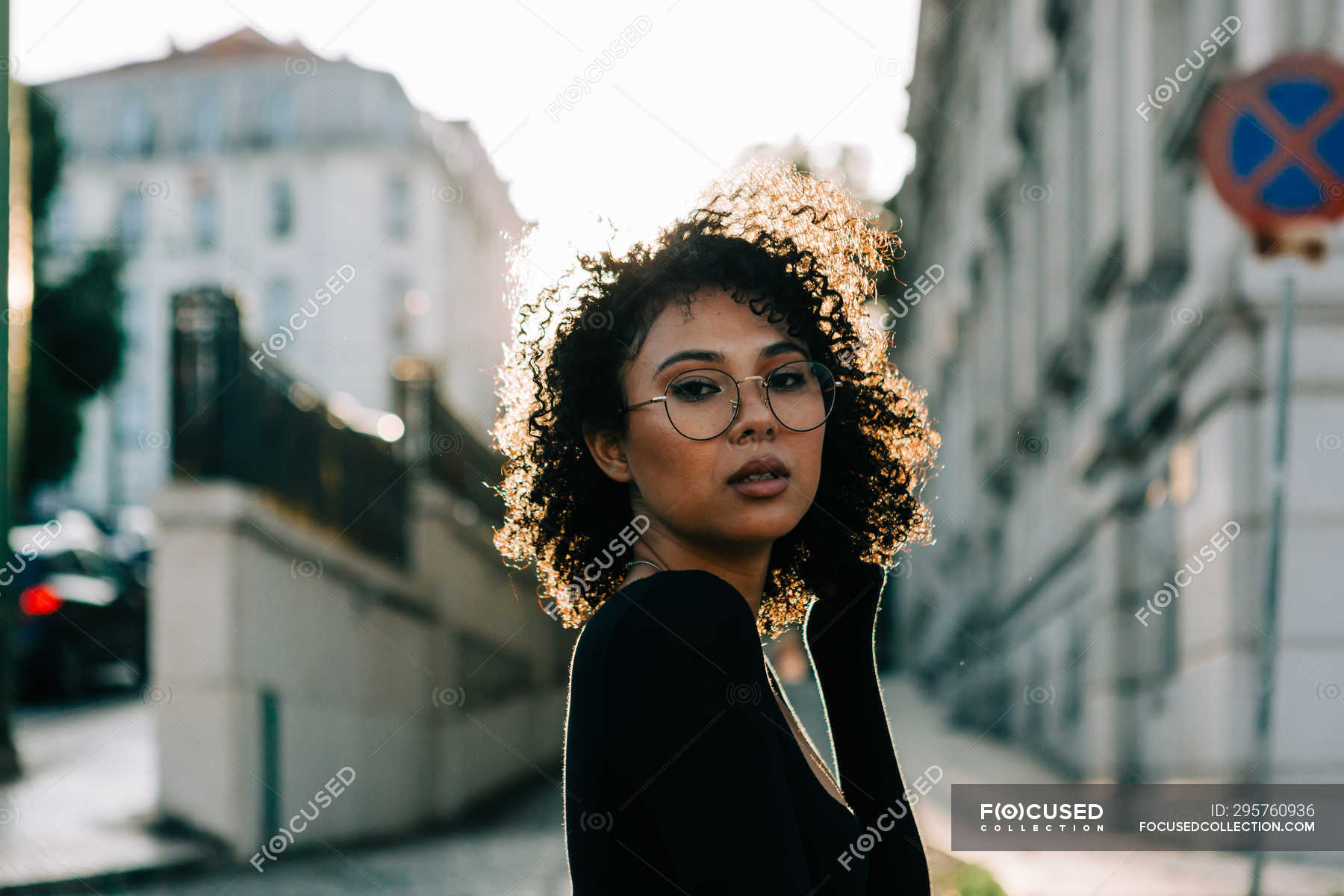 Fashionable African American woman in black top standing on sidewalk ...