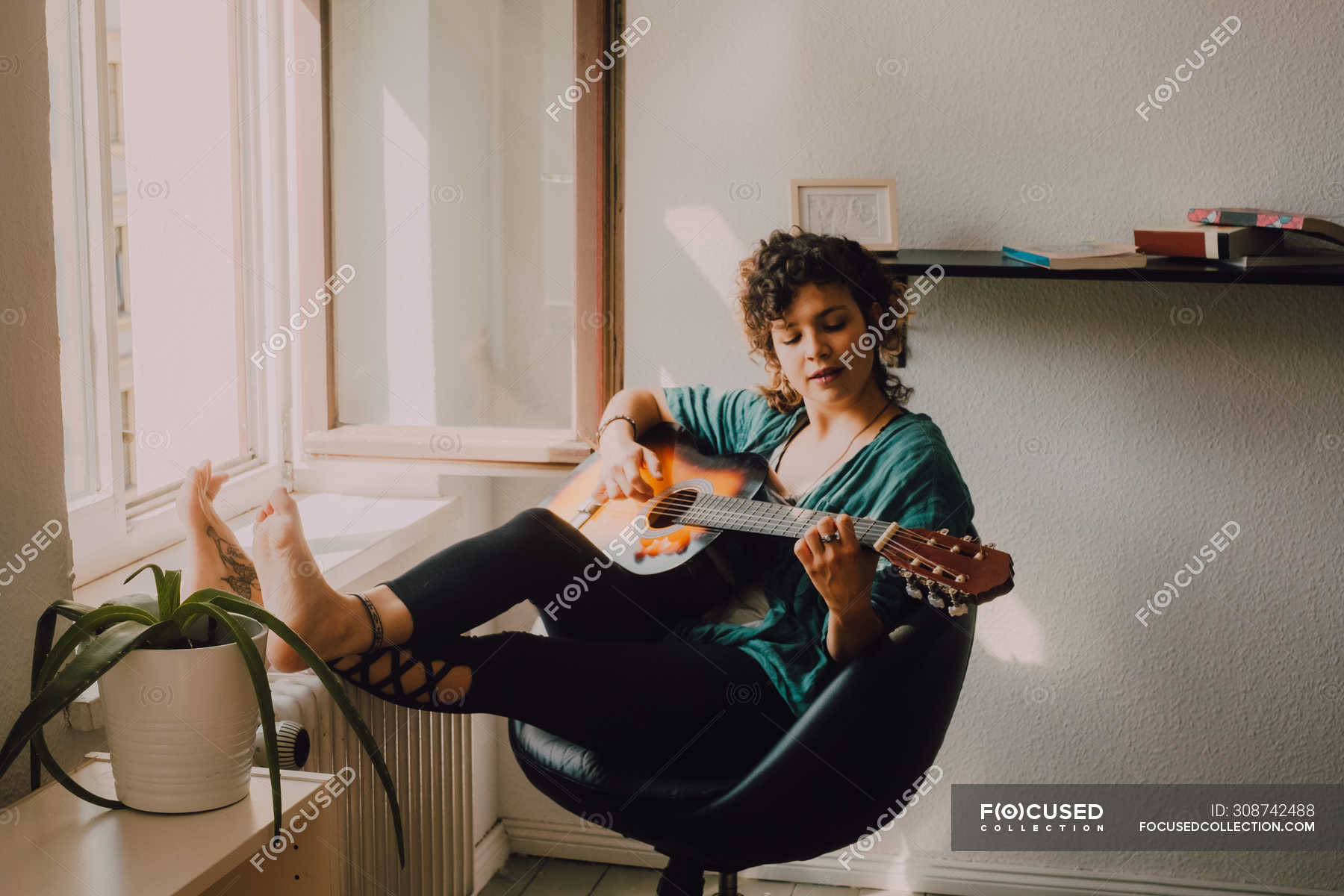 Donna rilassata a piedi nudi in abiti casual suonare la chitarra