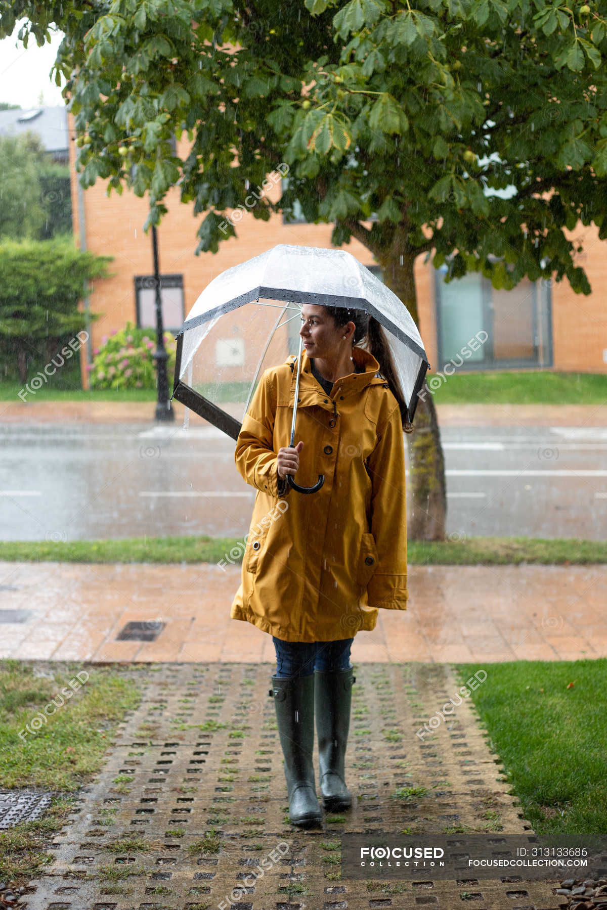 Chica joven con chubasquero amarillo con paraguas transparente en la  ciudad. Joven hermosa mujer con traje de lluvia y gafas mientras camina en  la calle. Con Fotografía de stock - Alamy