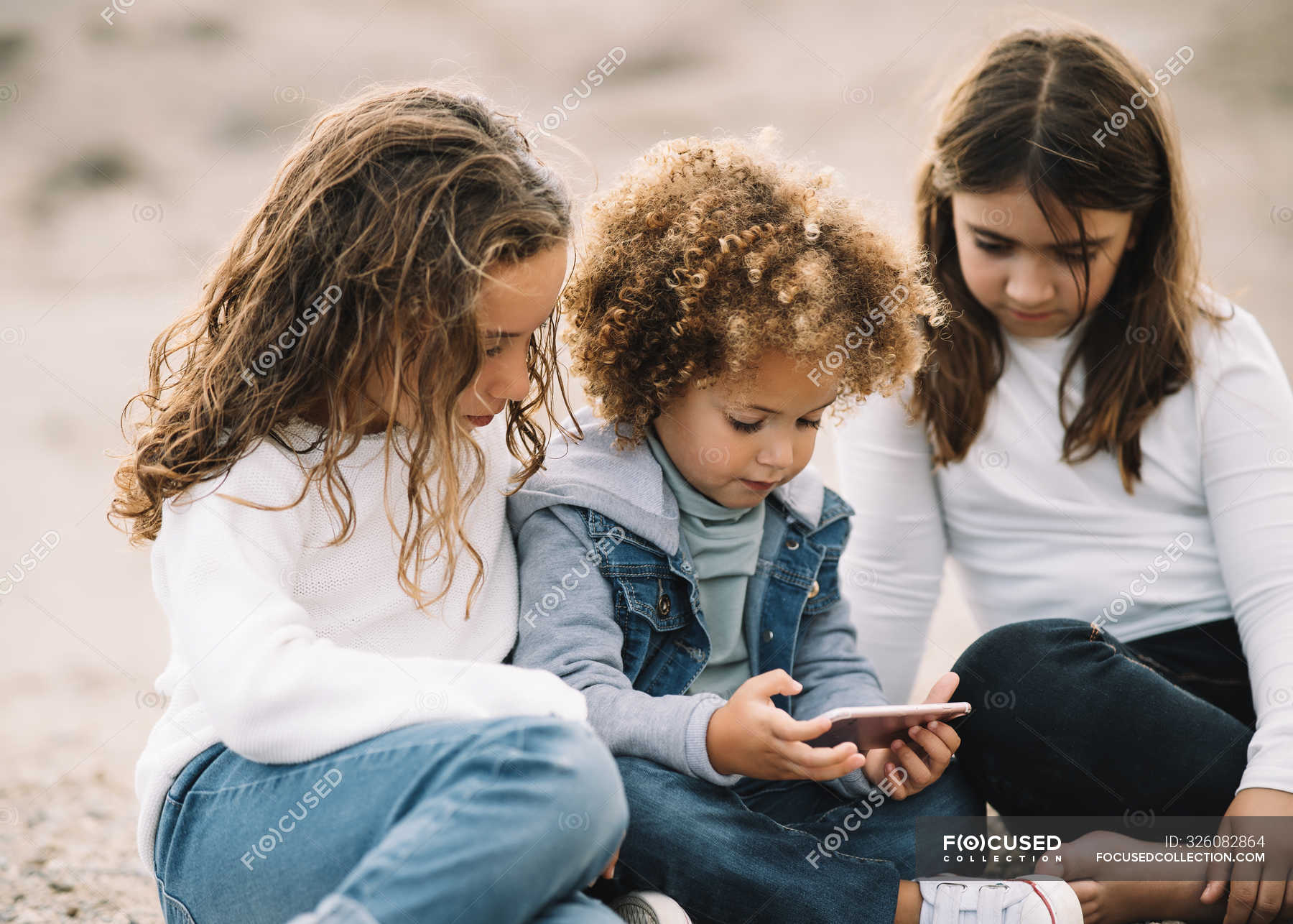 Concentrated Casual Mixed Race Kids Relaxing On Sand And Sharing