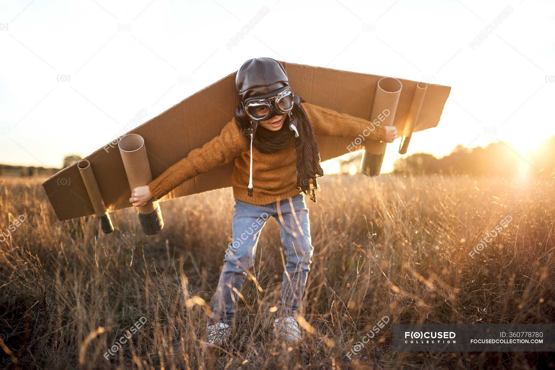 Happy kid in goggles and cardboard wings raising hands during game on
