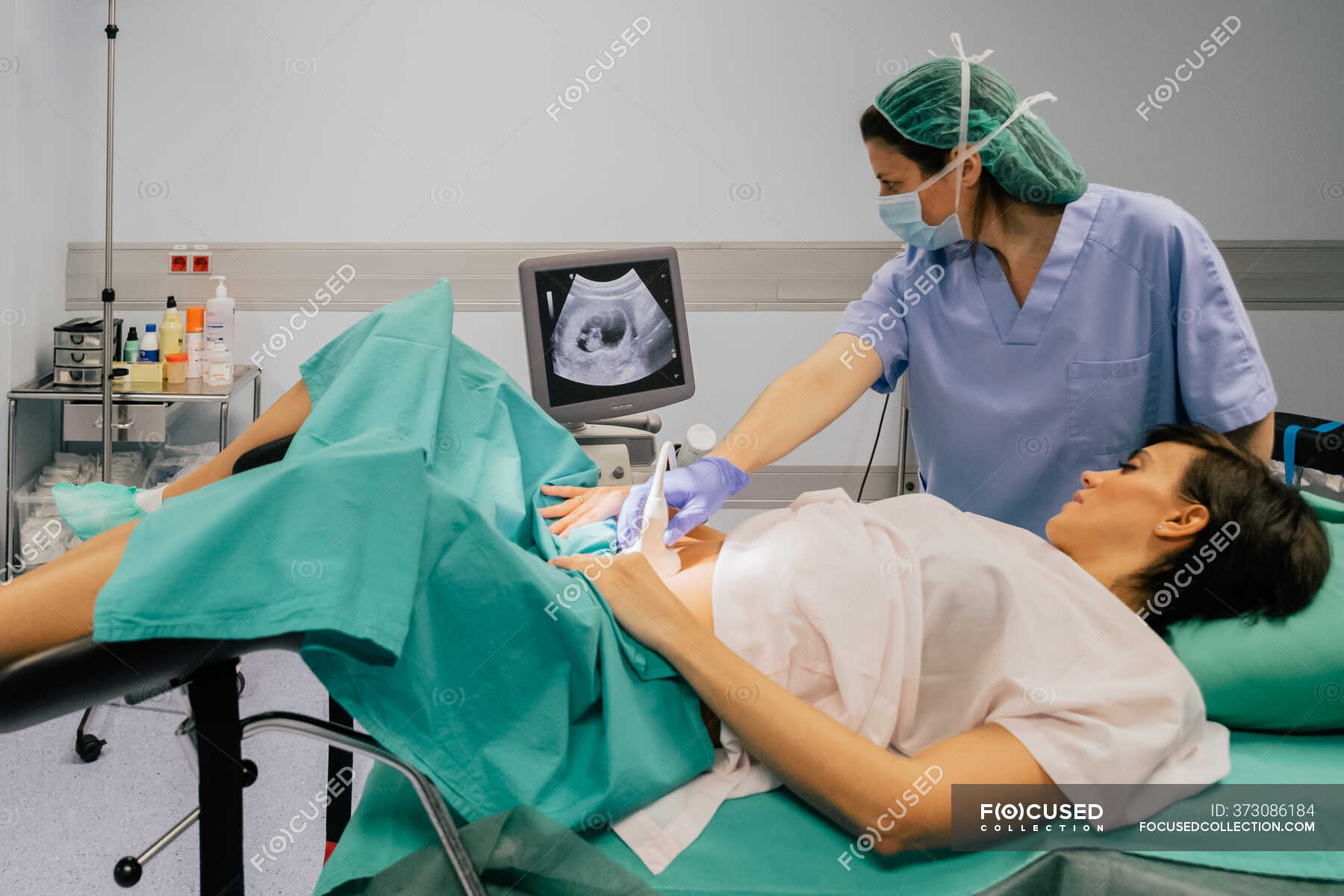 Female doctor in sterile mask and blue glove using ultrasound scanner