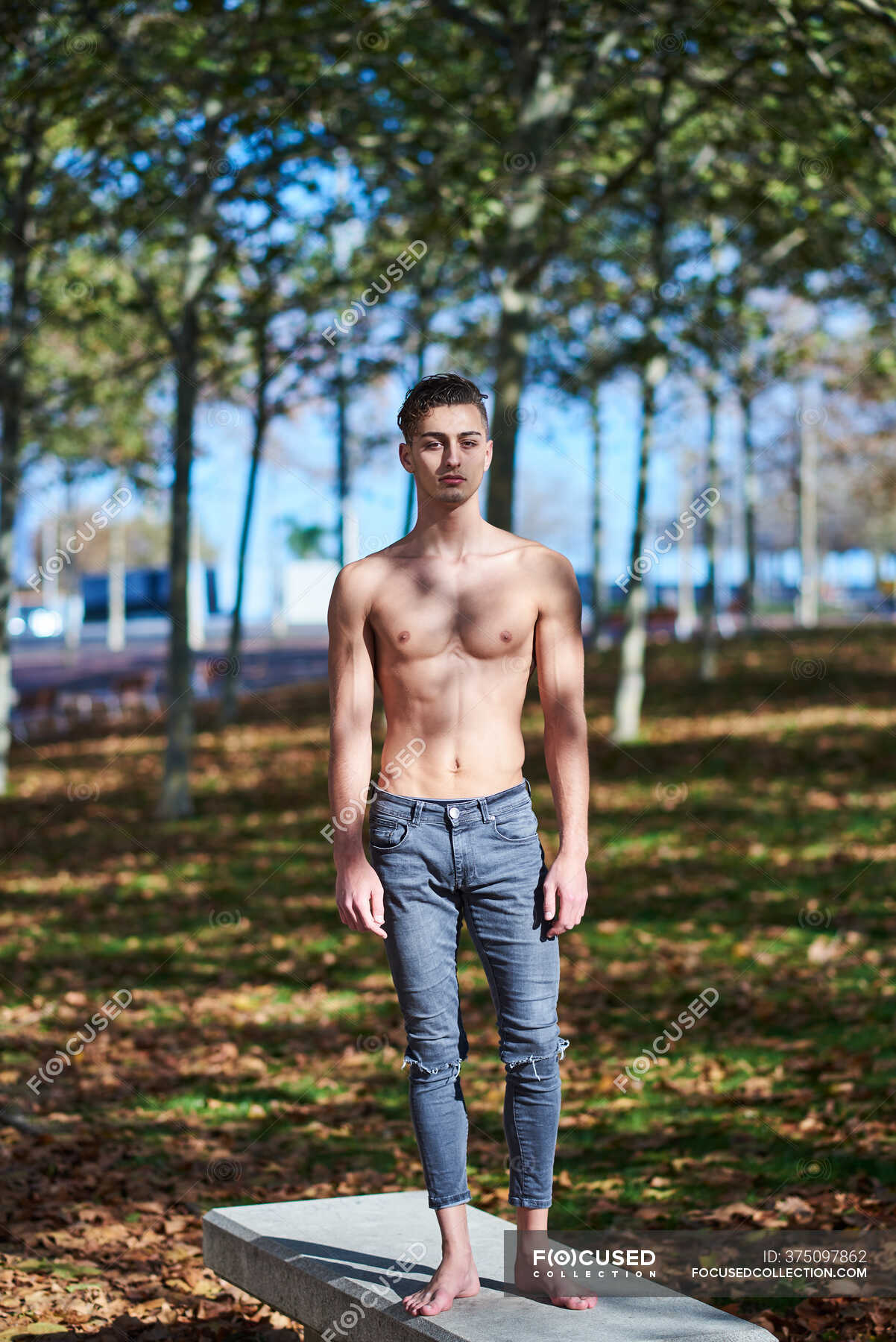 Full Body Shirtless Male Athlete In Ripped Jeans Standing On Concrete Bench And Looking At