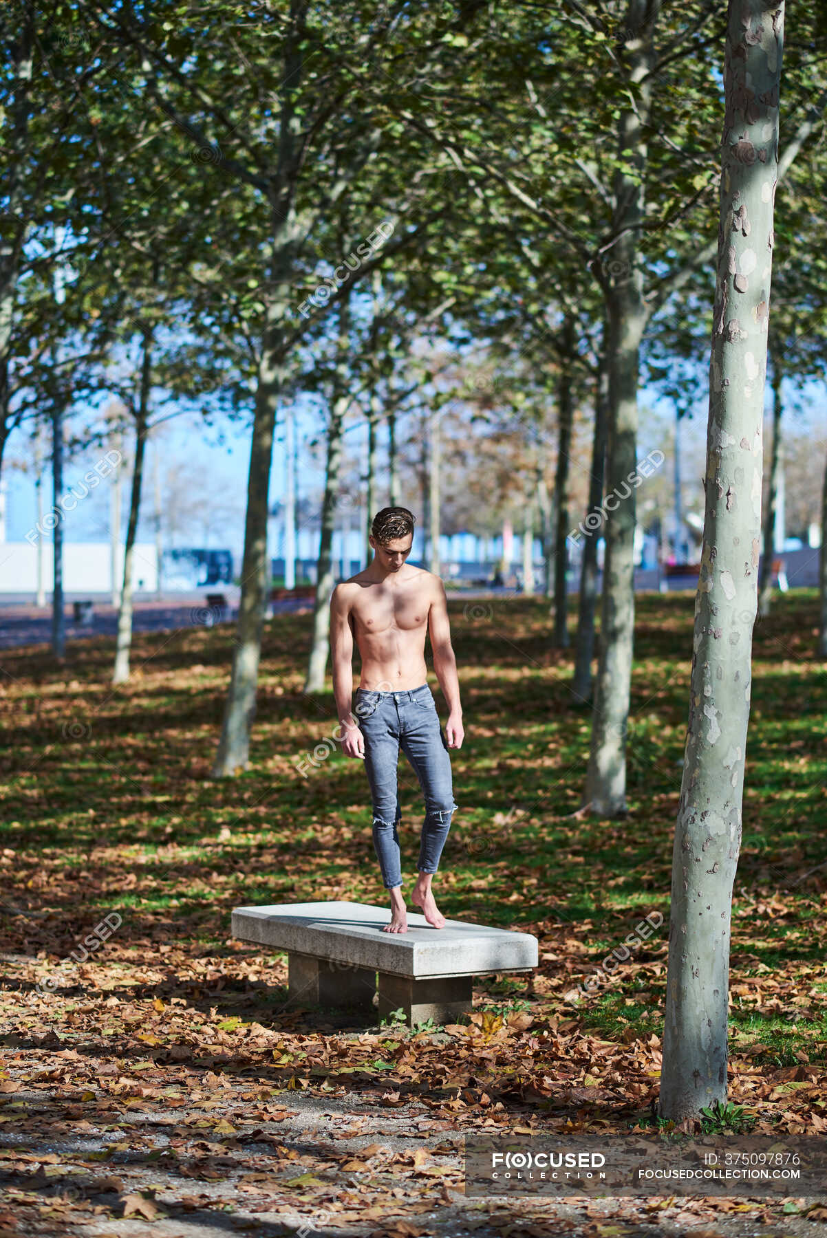 Full Body Shirtless Male Athlete In Ripped Jeans Standing On Concrete Bench And Looking Down