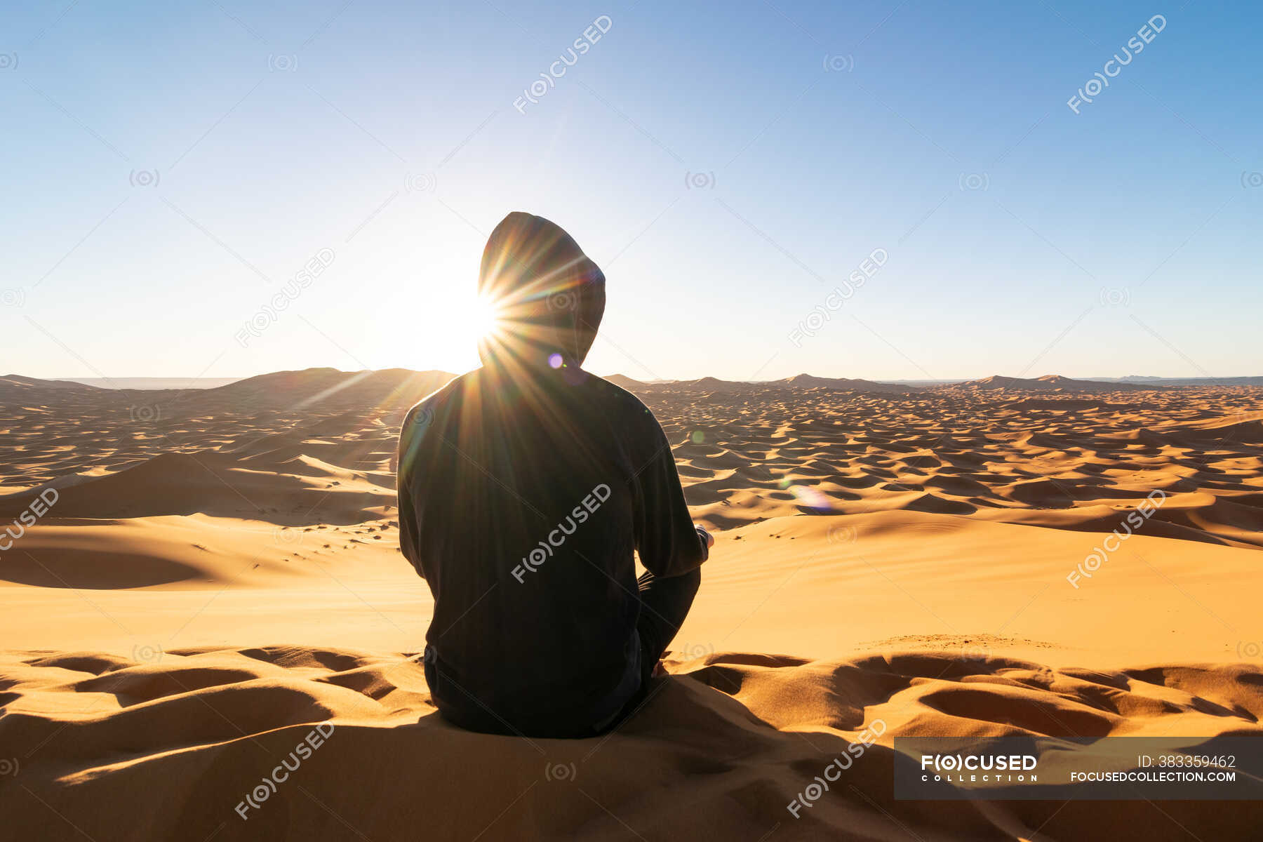 Back view of unrecognizable tourist sitting on sand dune and admiring ...