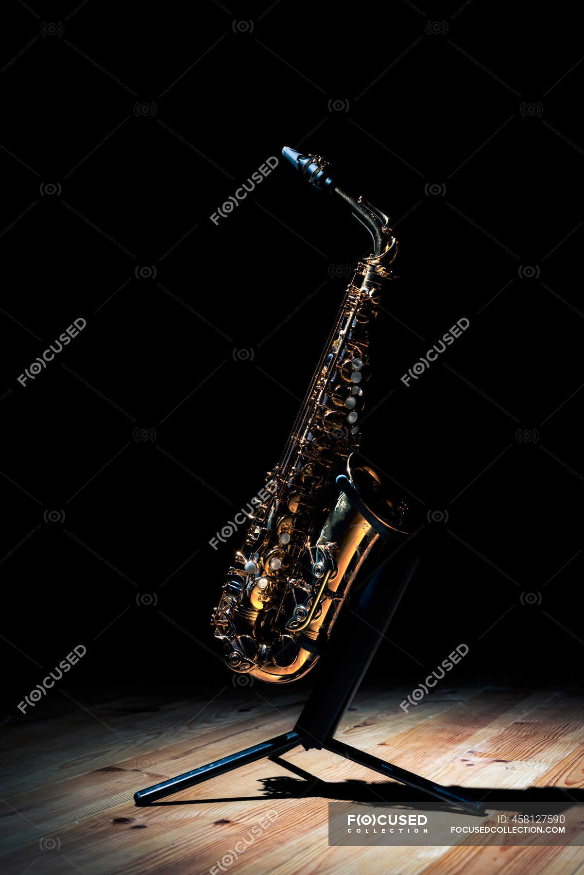 Shiny golden tenor saxophone on stand placed on wooden stage against ...