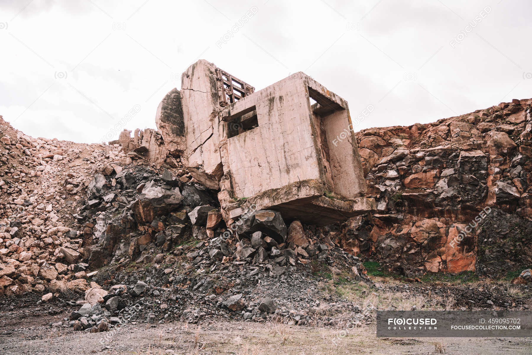 Piece Of Destroyed Cement Building On Open Pit With Rough Stones Under Cloudy Sky In Daylight