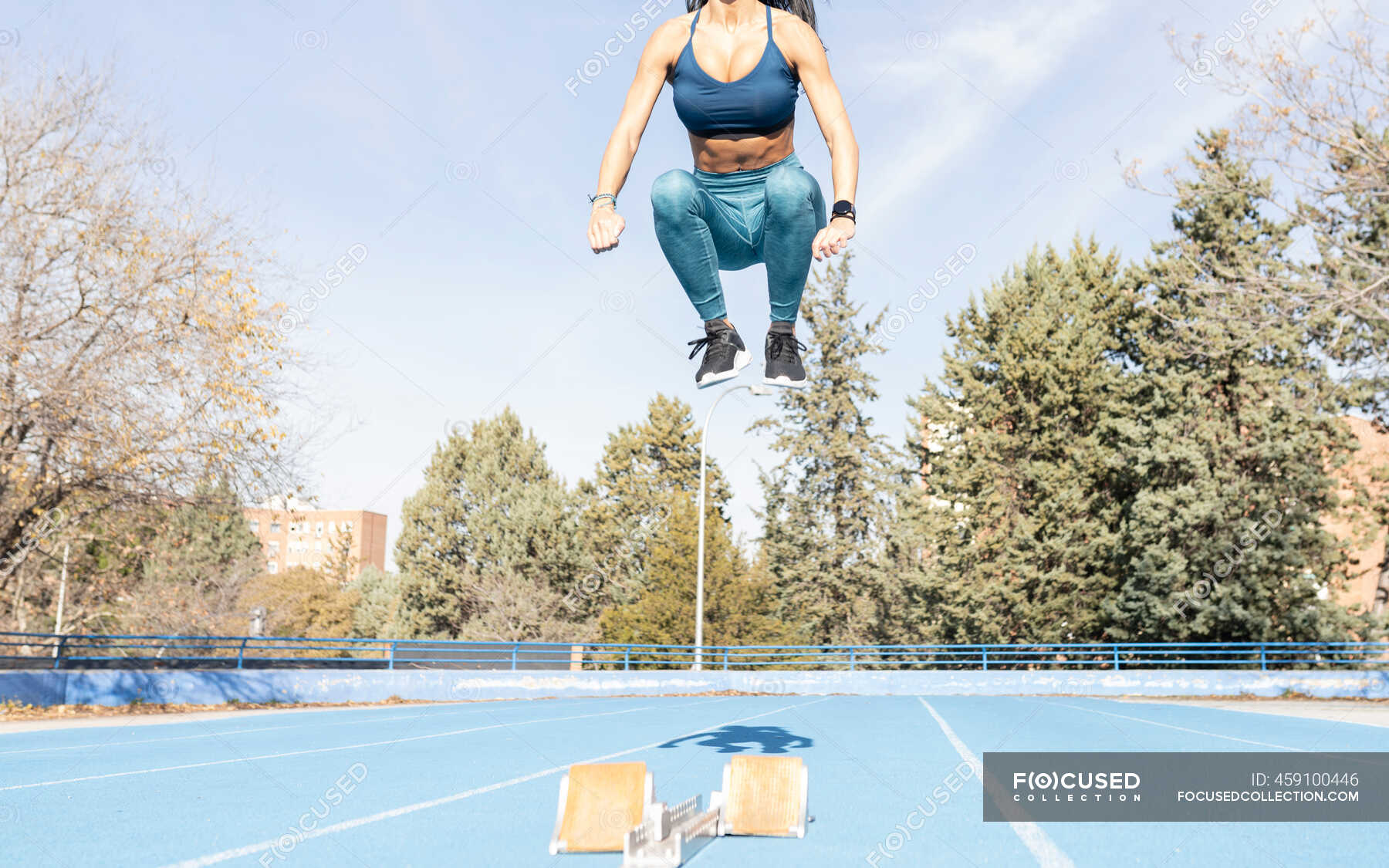 Determined female runner jumping above track with starting blocks while