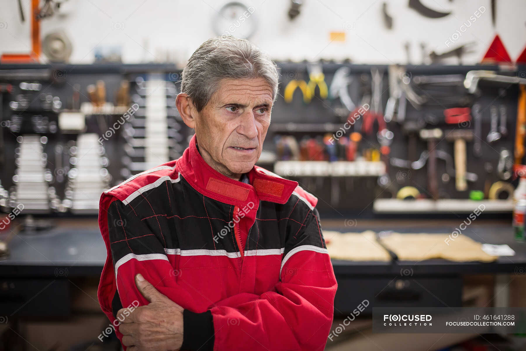 Serious senior male mechanic in red workwear standing in repair service ...