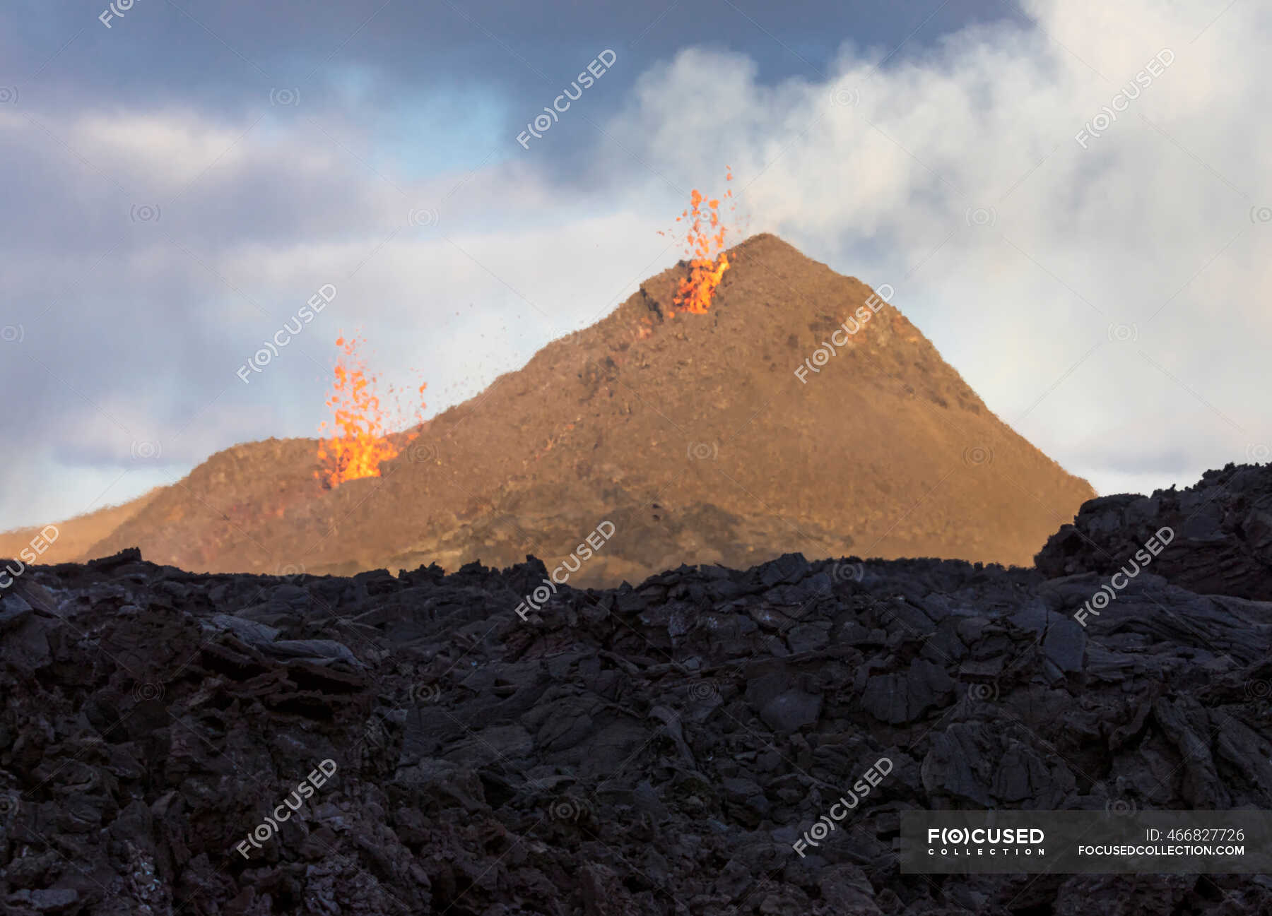 Side view of magma sparks out of the volcano hole and run like rivers of lava over the ground in