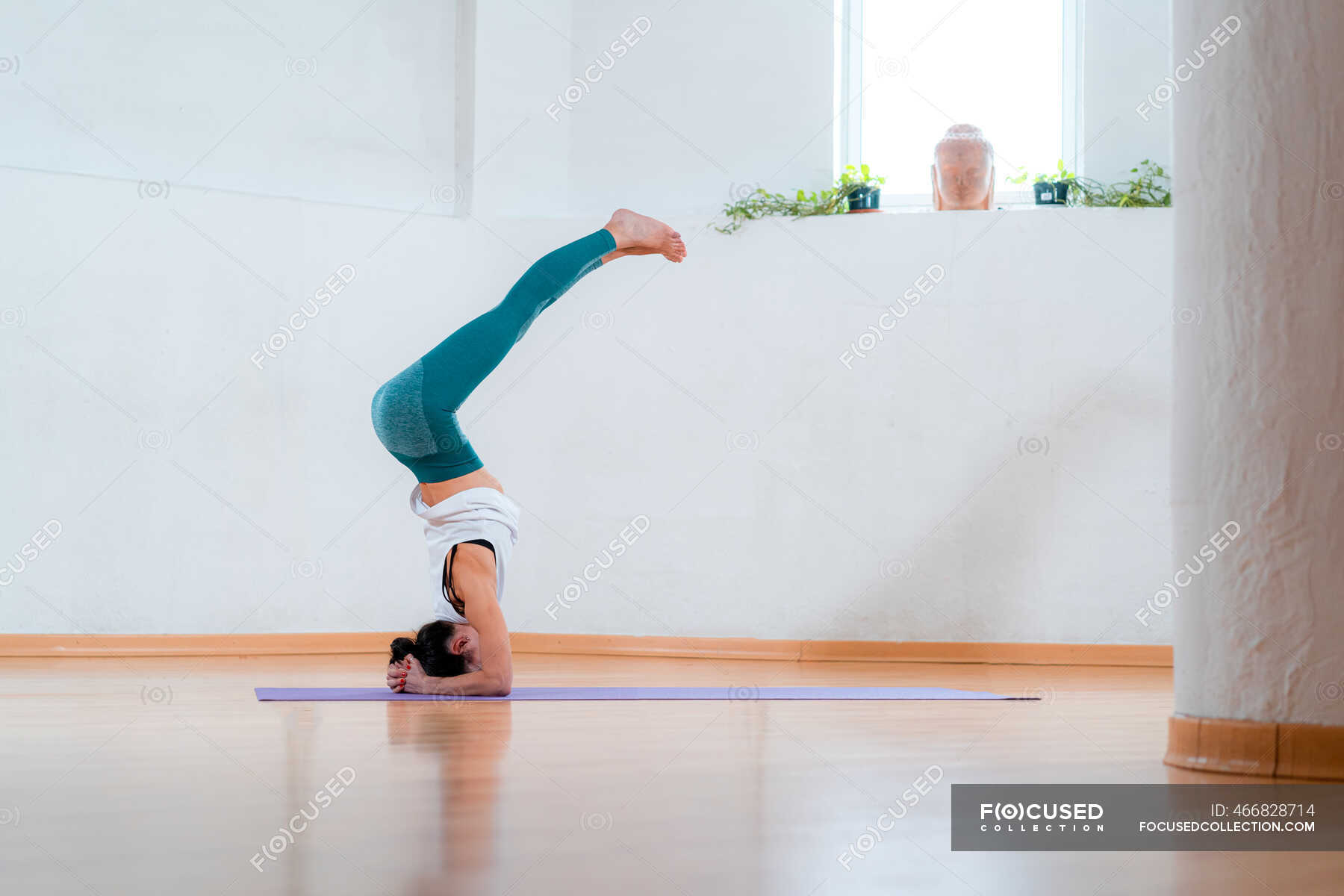 Side view of anonymous flexible female in sportswear standing on head ...