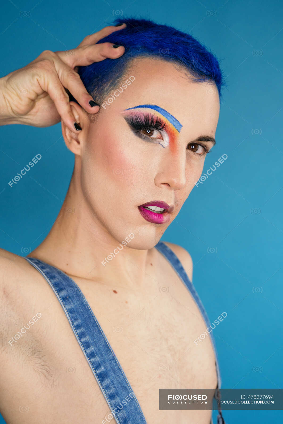 Calm Young Homosexual Male With Dyed Blue Hair And Drag Makeup On Half Face Standing On Blue Background And Looking At Camera Lgbt Accept Stock Photo