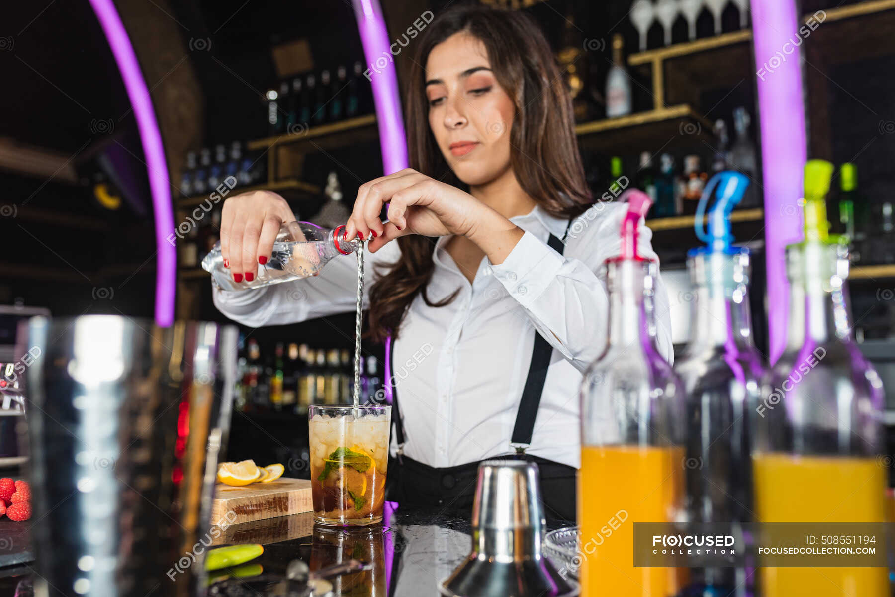 Female barkeeper in stylish outfit adding liquid from bottle into glass and  stirring with long spoon while preparing cocktail standing at counter in  modern bar — fashion, people - Stock Photo | #508551194