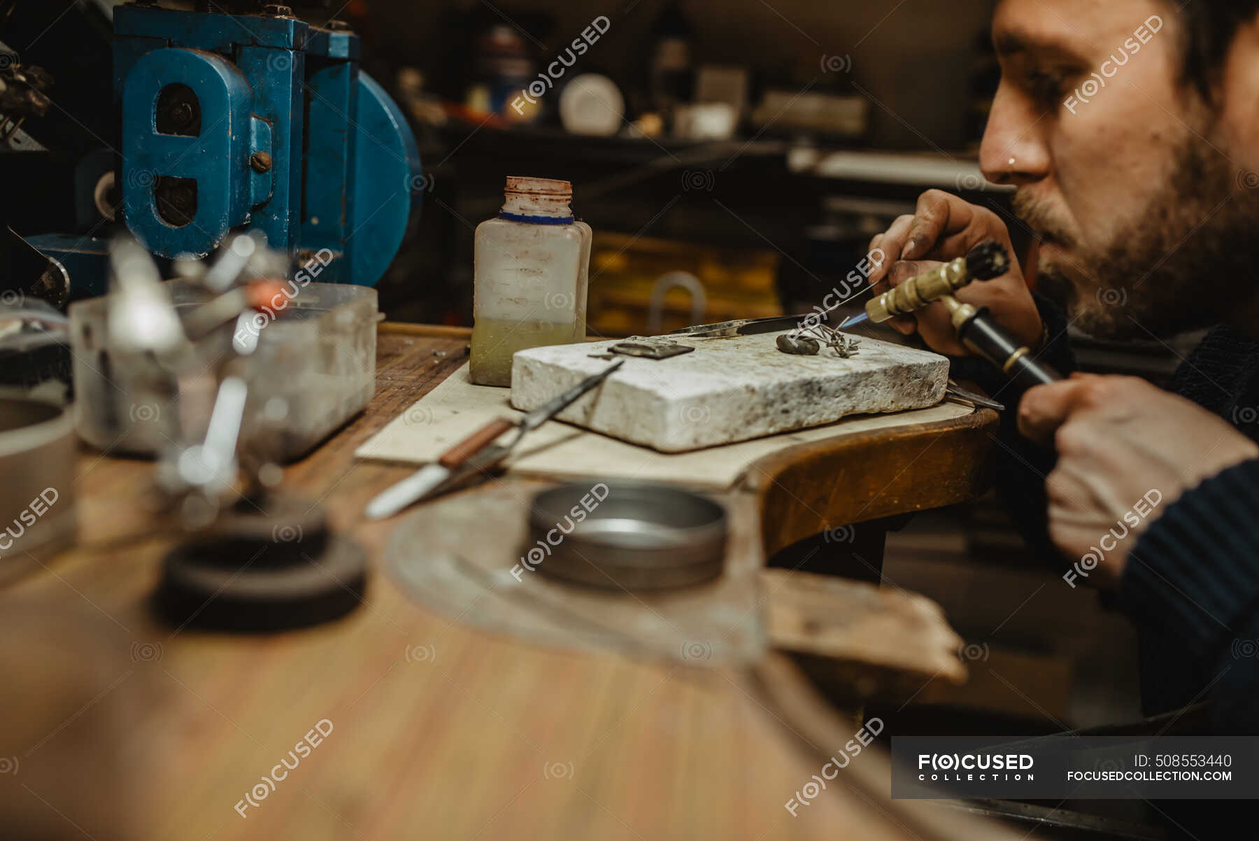 Goldsmith using blowtorch to heat tiny metal ornament while making