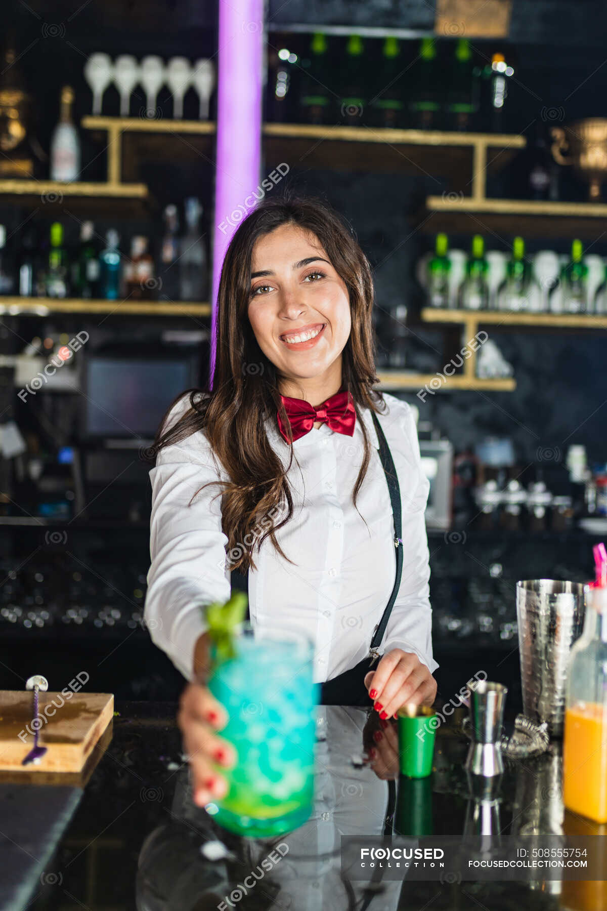 Happy female barkeeper in stylish outfit serving blue cocktail with mint  while standing at counter in modern bar — blur, Waitress - Stock Photo |  #508555754