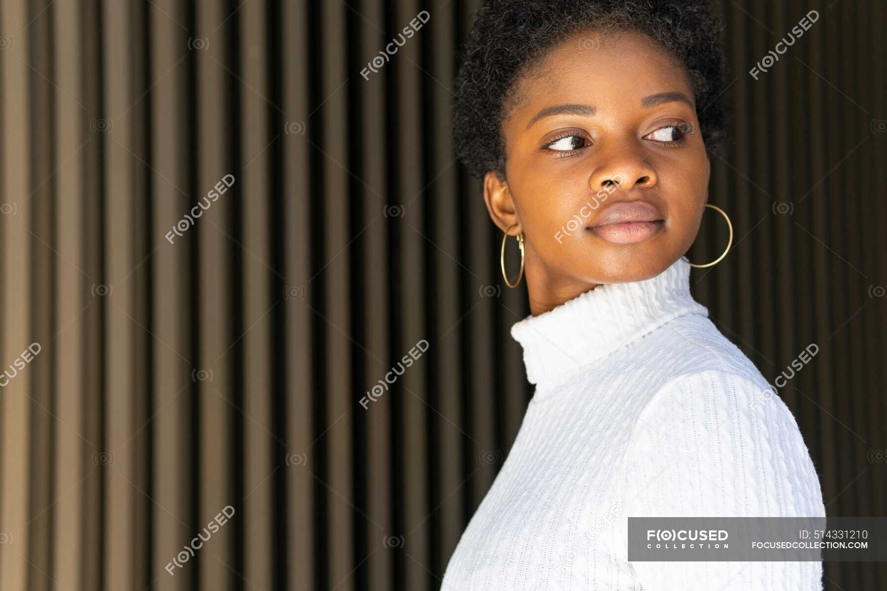 Side View Of Unemotional African American Female In Trendy Sweater Looking Away Against Striped