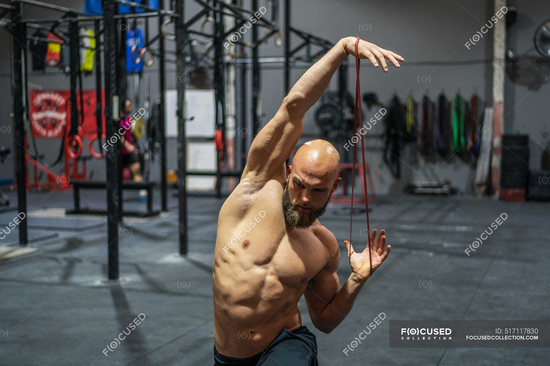 Shirtless bearded man looking away stretching elastic band with arms