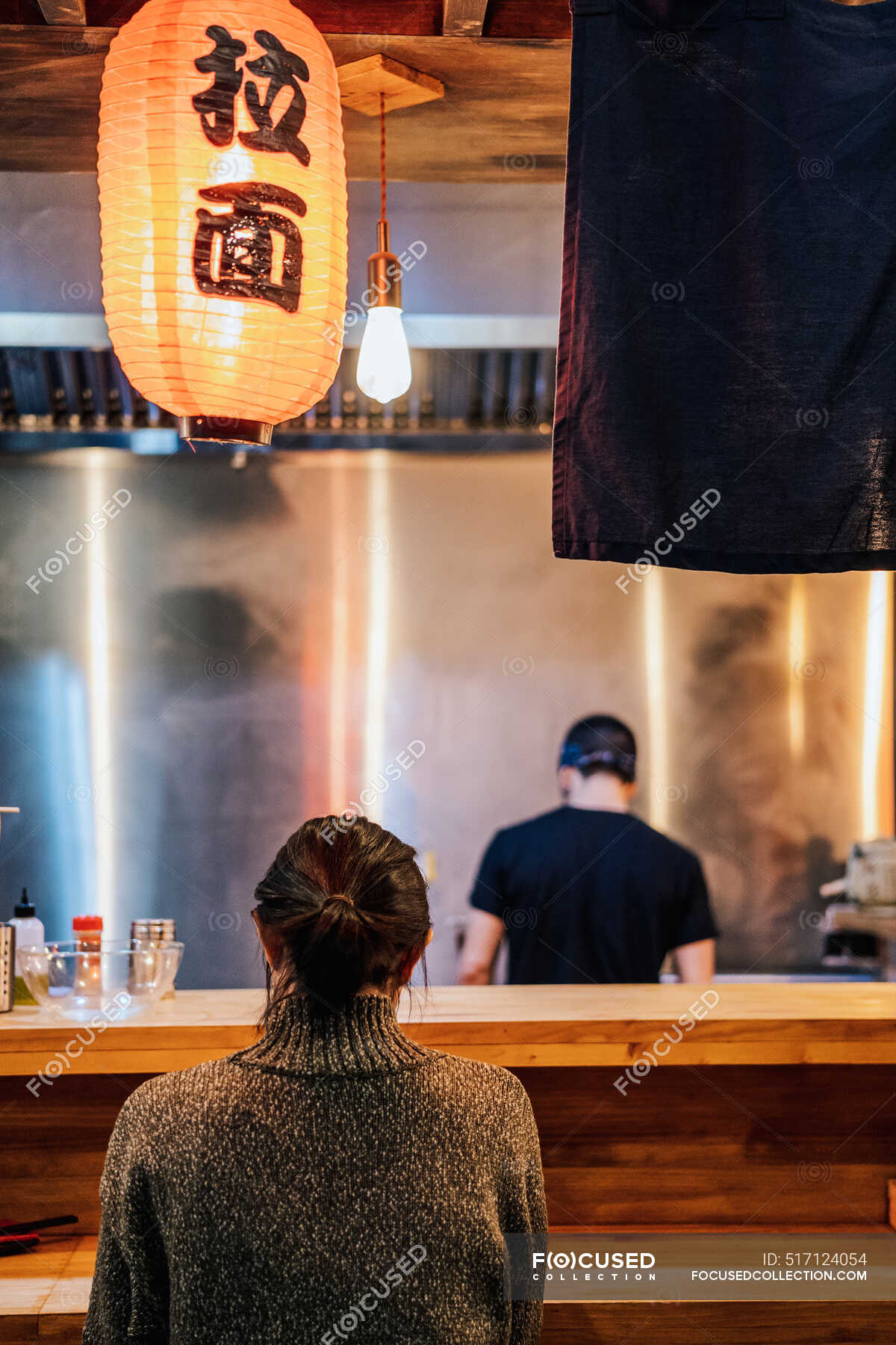 Back view of faceless black haired woman in sweater sitting at counter ...