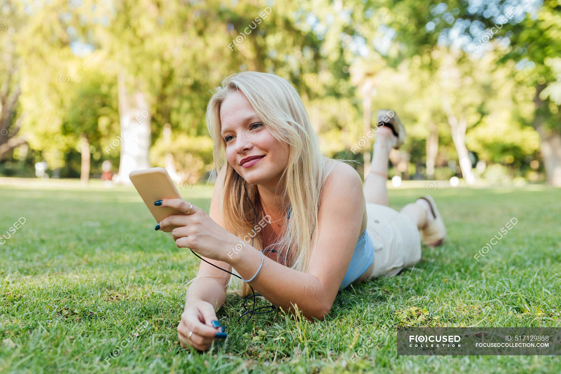 Smiling charming female lying on grass in park taking selfie on ...