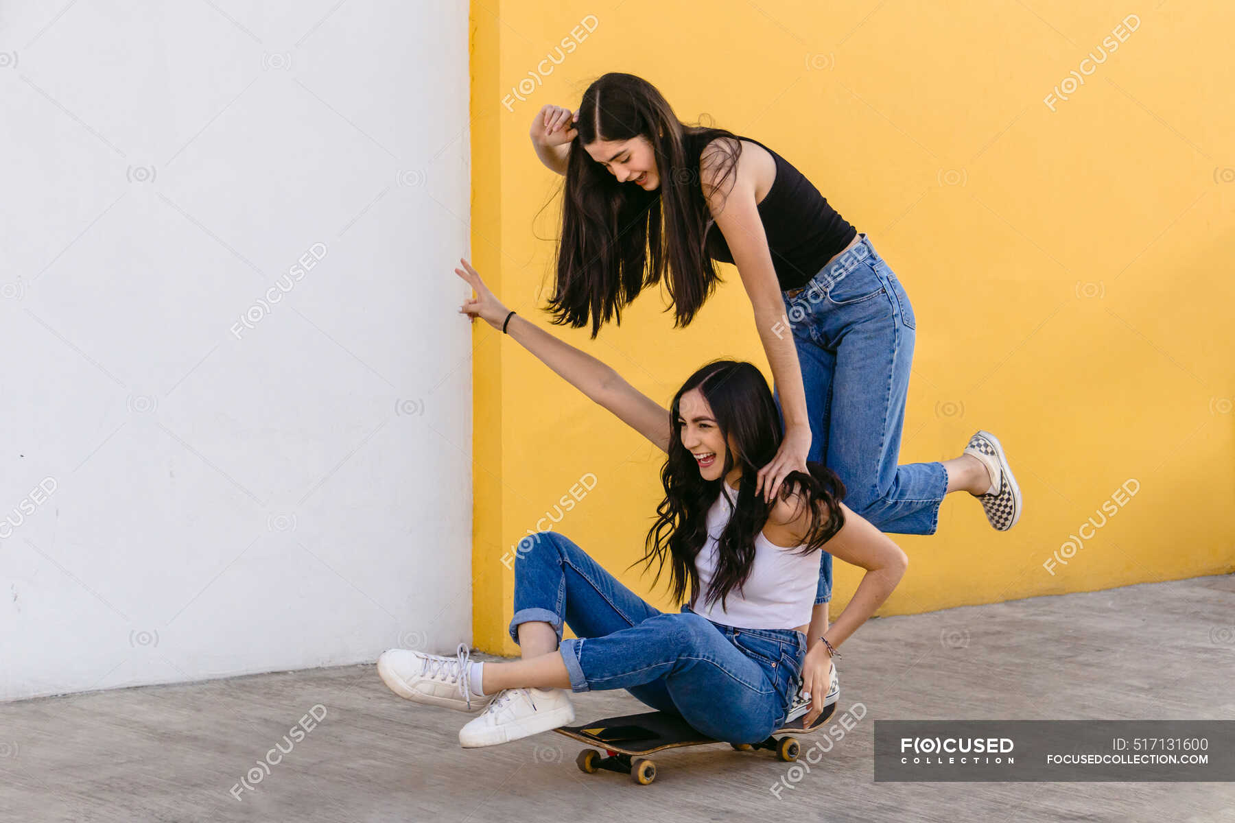 Cheerful teen with crossed legs riding skateboard with content female